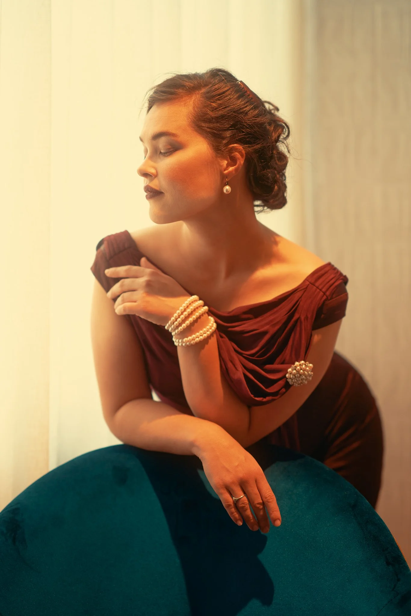Anita in a burgundy dress leaning on a teal velvet chair