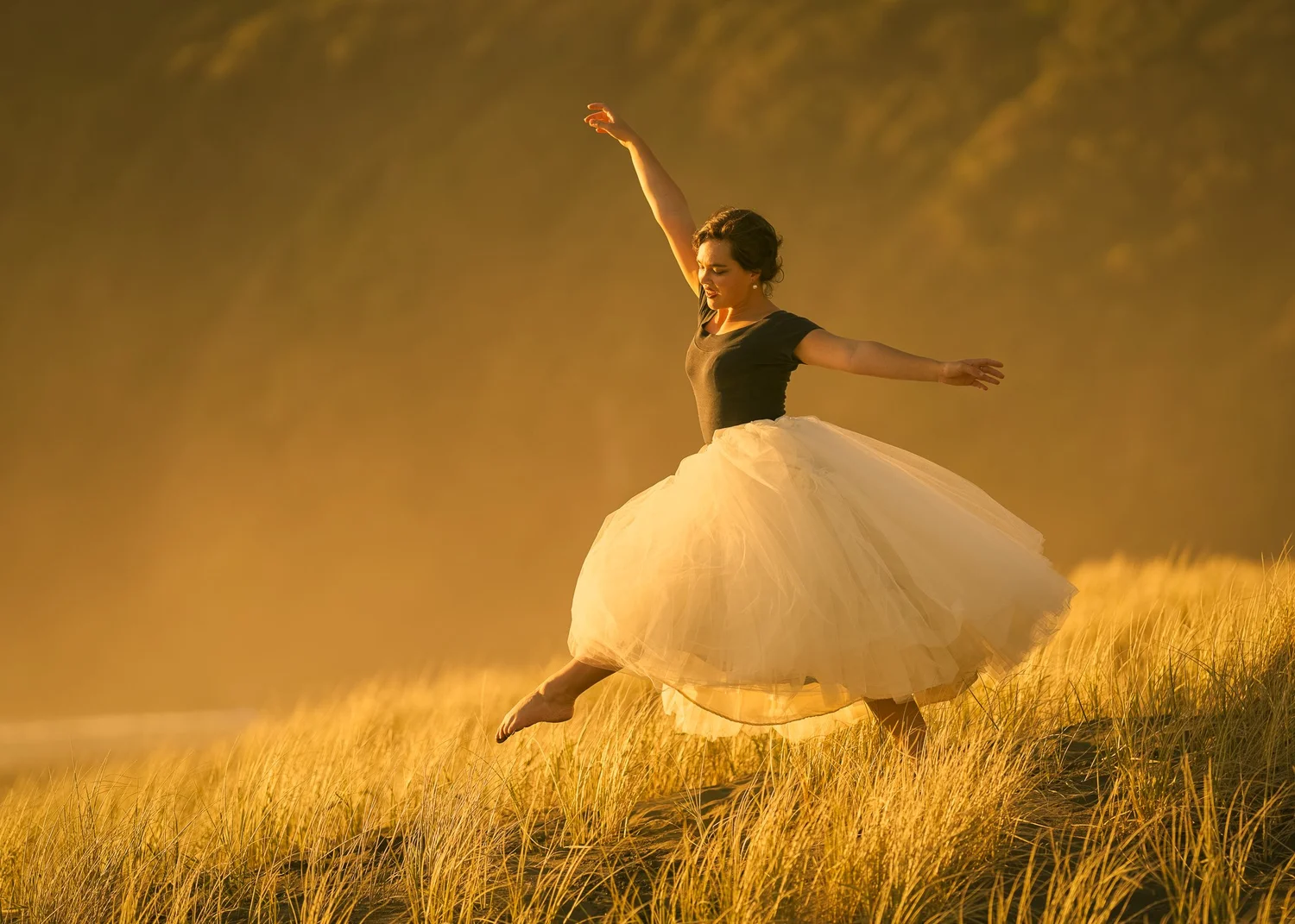 Anita dances in a full tulle skirt across golden grass at sunset