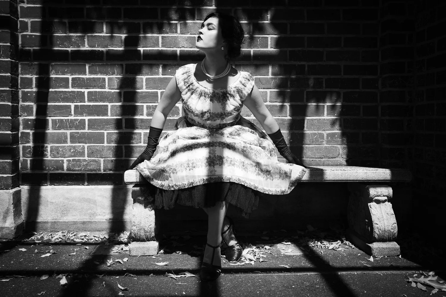 Black and white photo of Anita on a bench against a brick wall in strong shadows