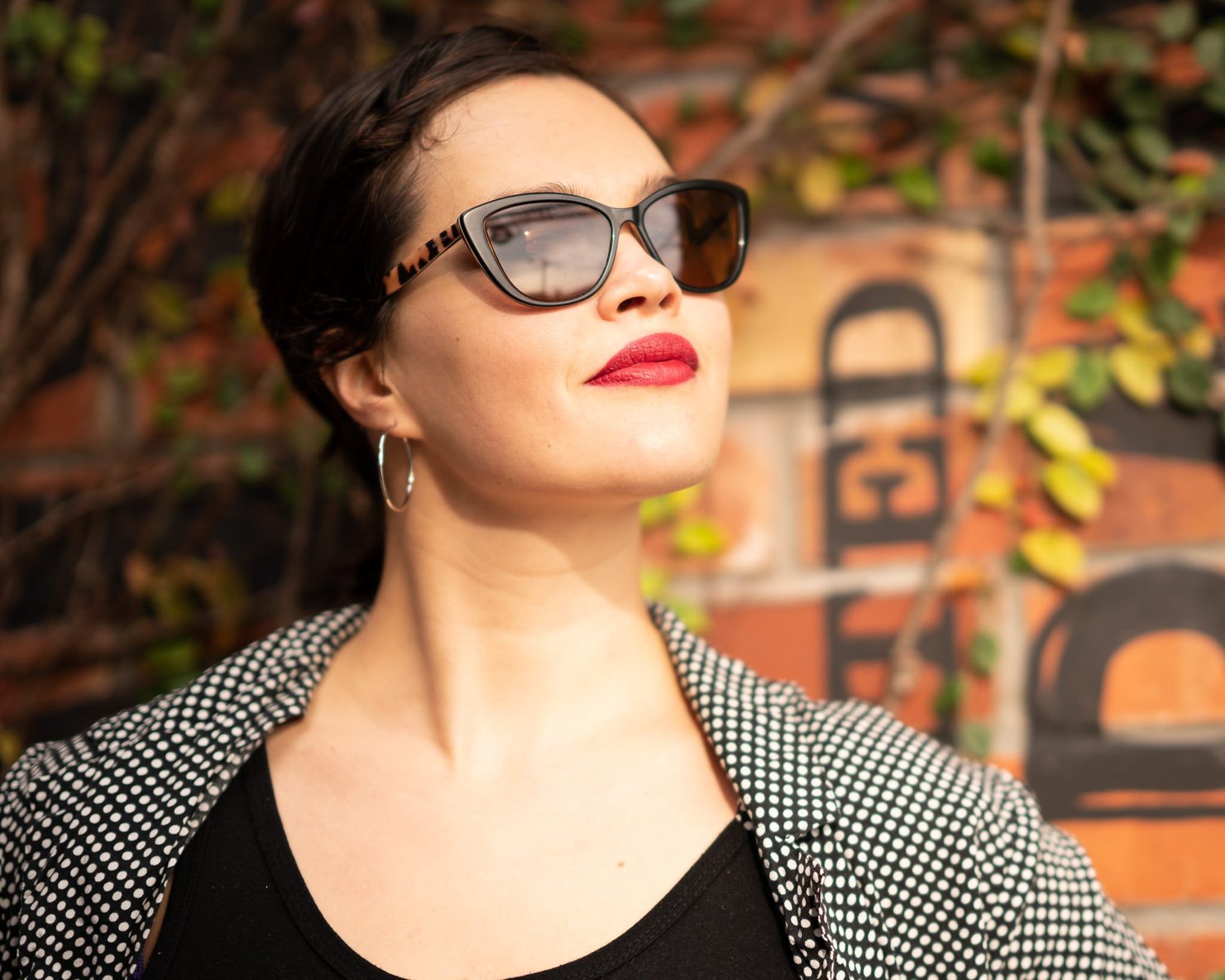 Anita in sunglasses in front of a painted brick wall