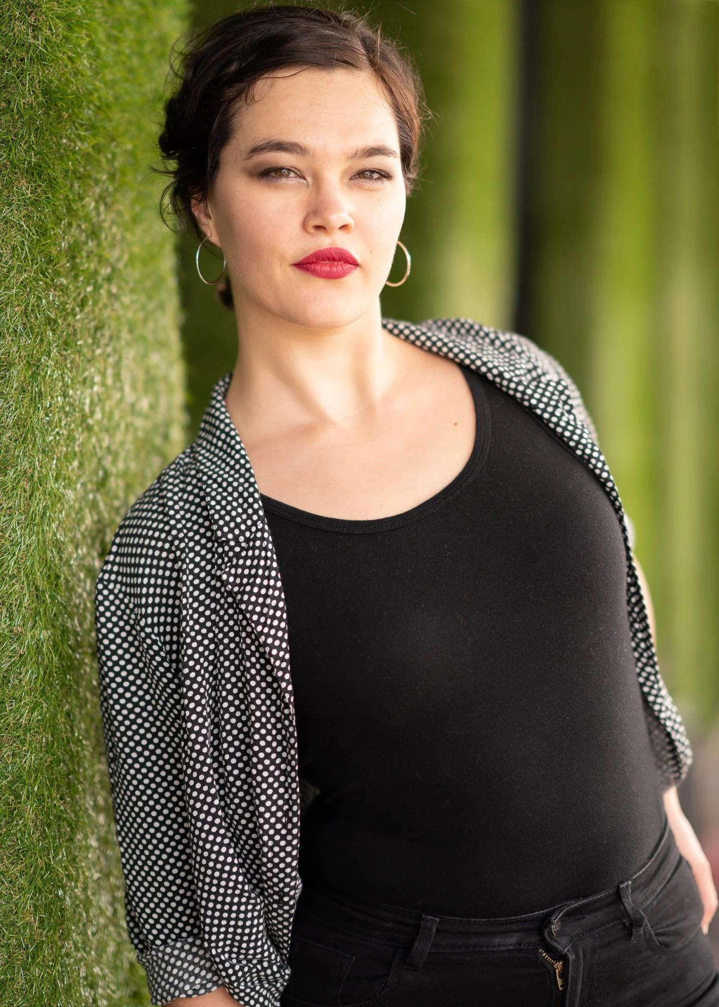 Anita in a black top and checked jacket against green foliage