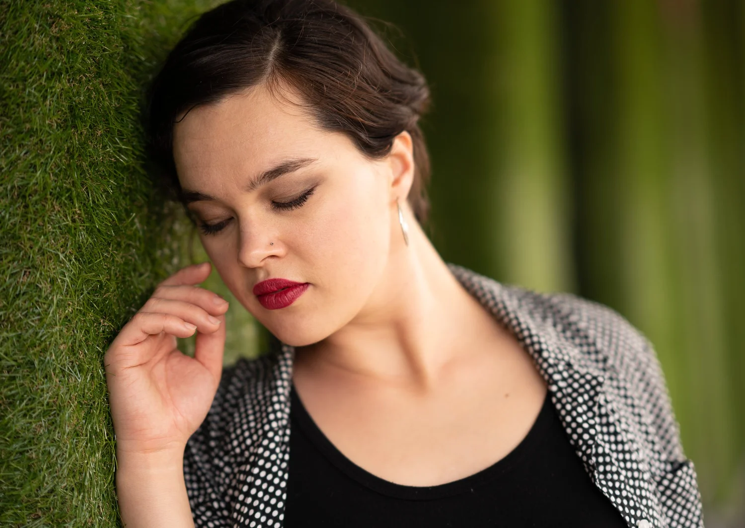 Anita with eyes closed leaning against a green wall