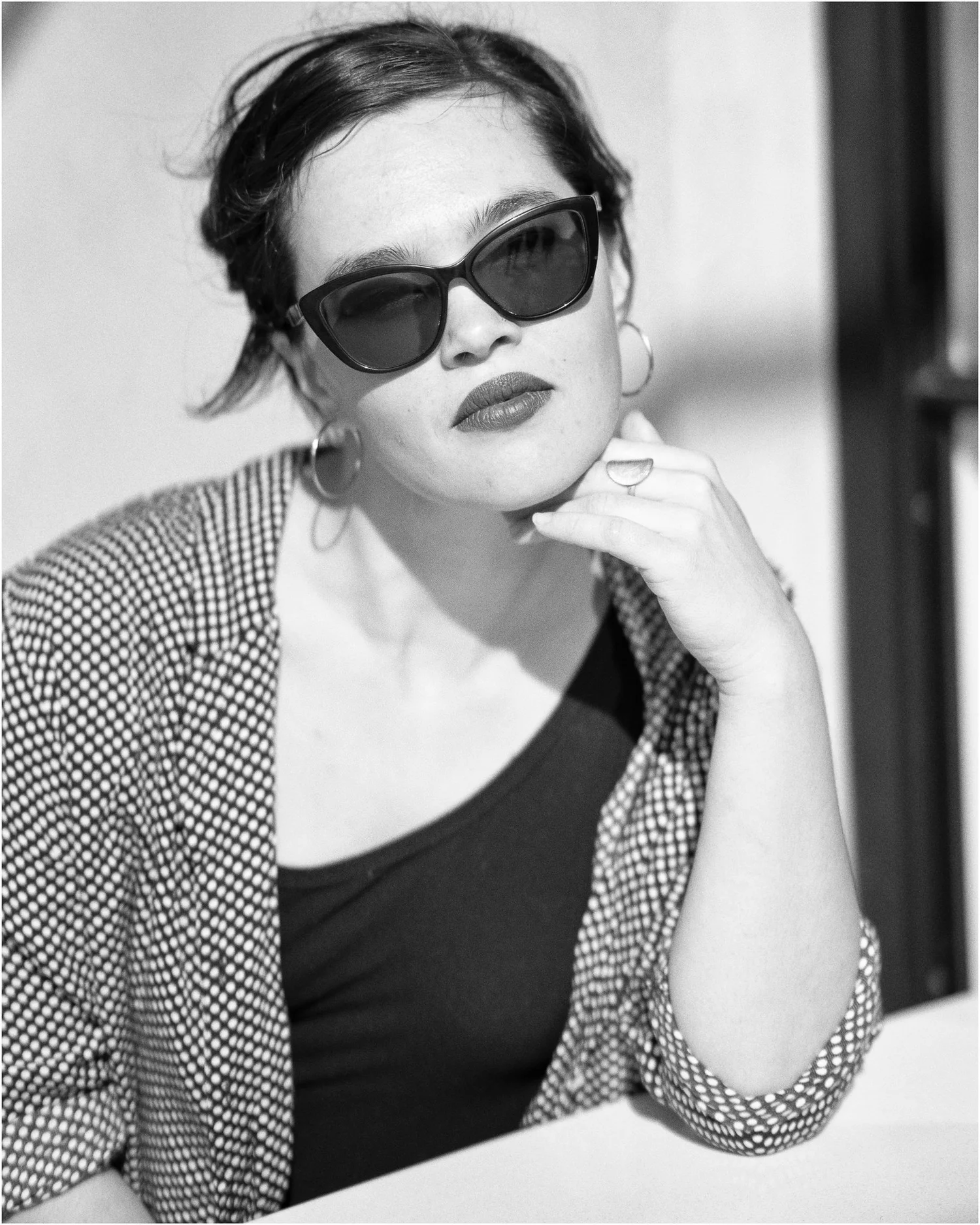 Black and white photo of Anita in sunglasses resting her chin on her hand