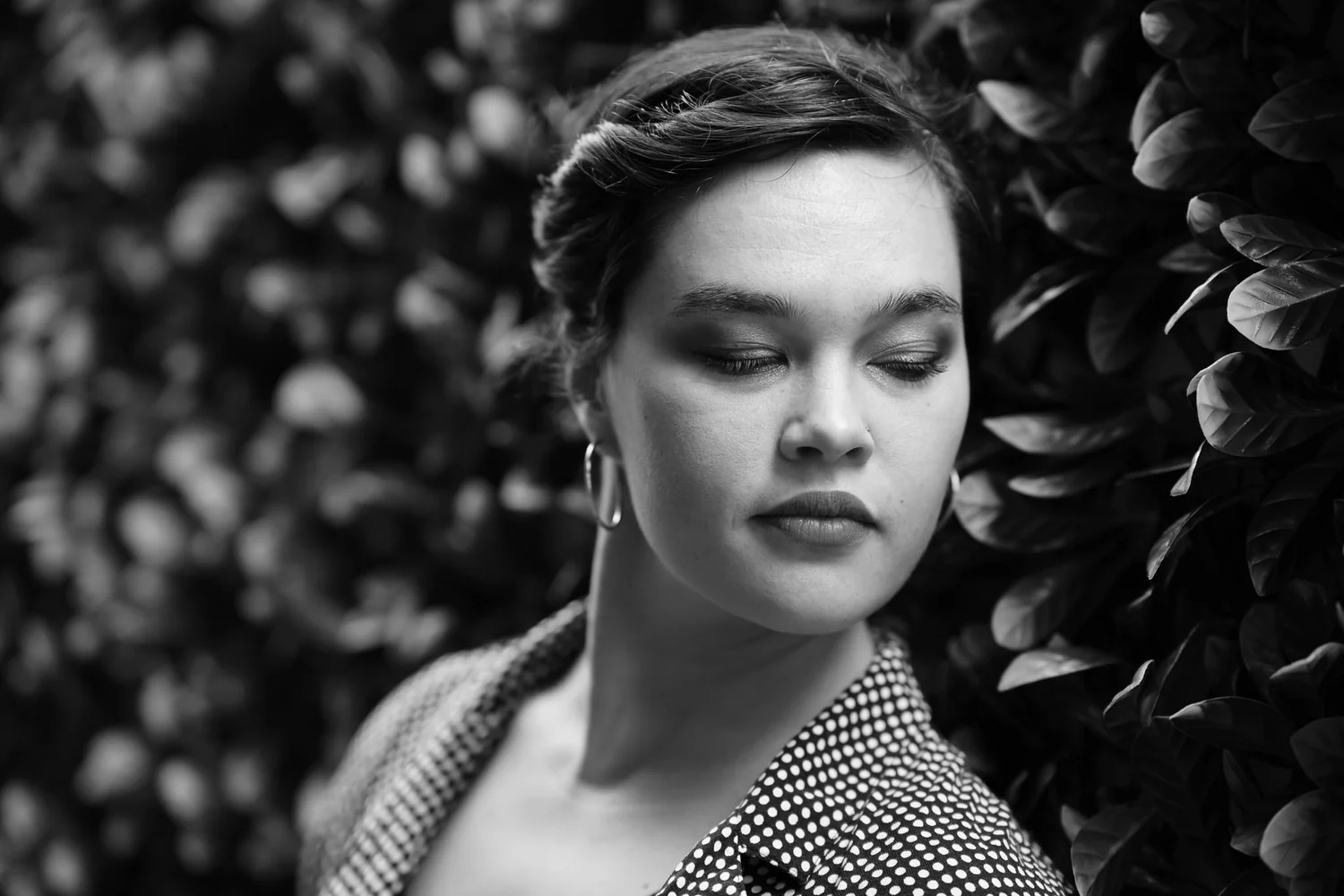 Black and white photo of Anita with eyes closed in front of leaves
