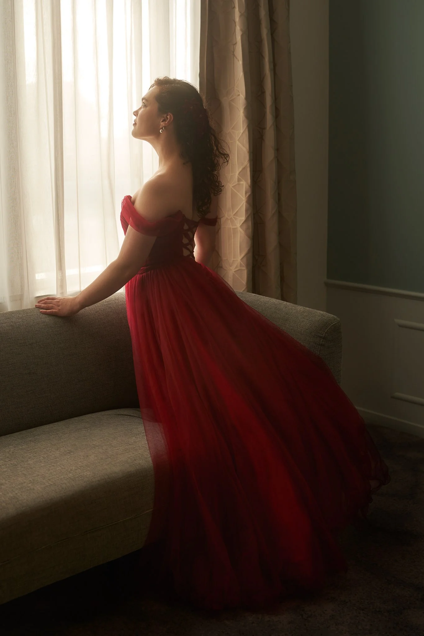 Anita in a red gown standing at a window with soft light