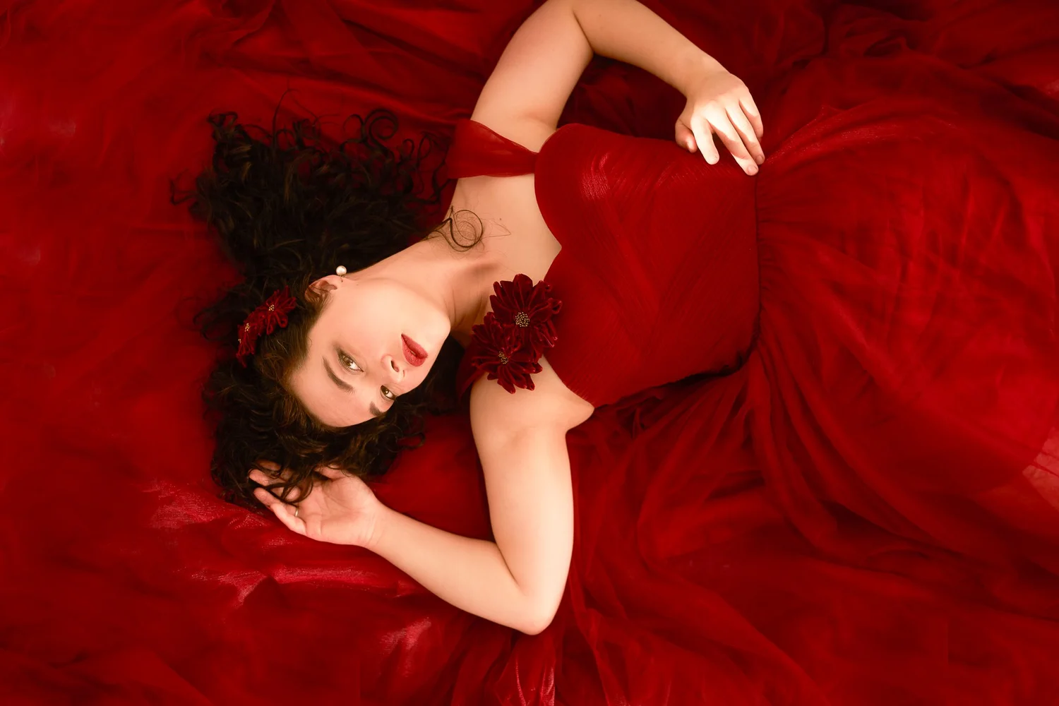 Anita lies on a bed of red fabric looking up at the camera