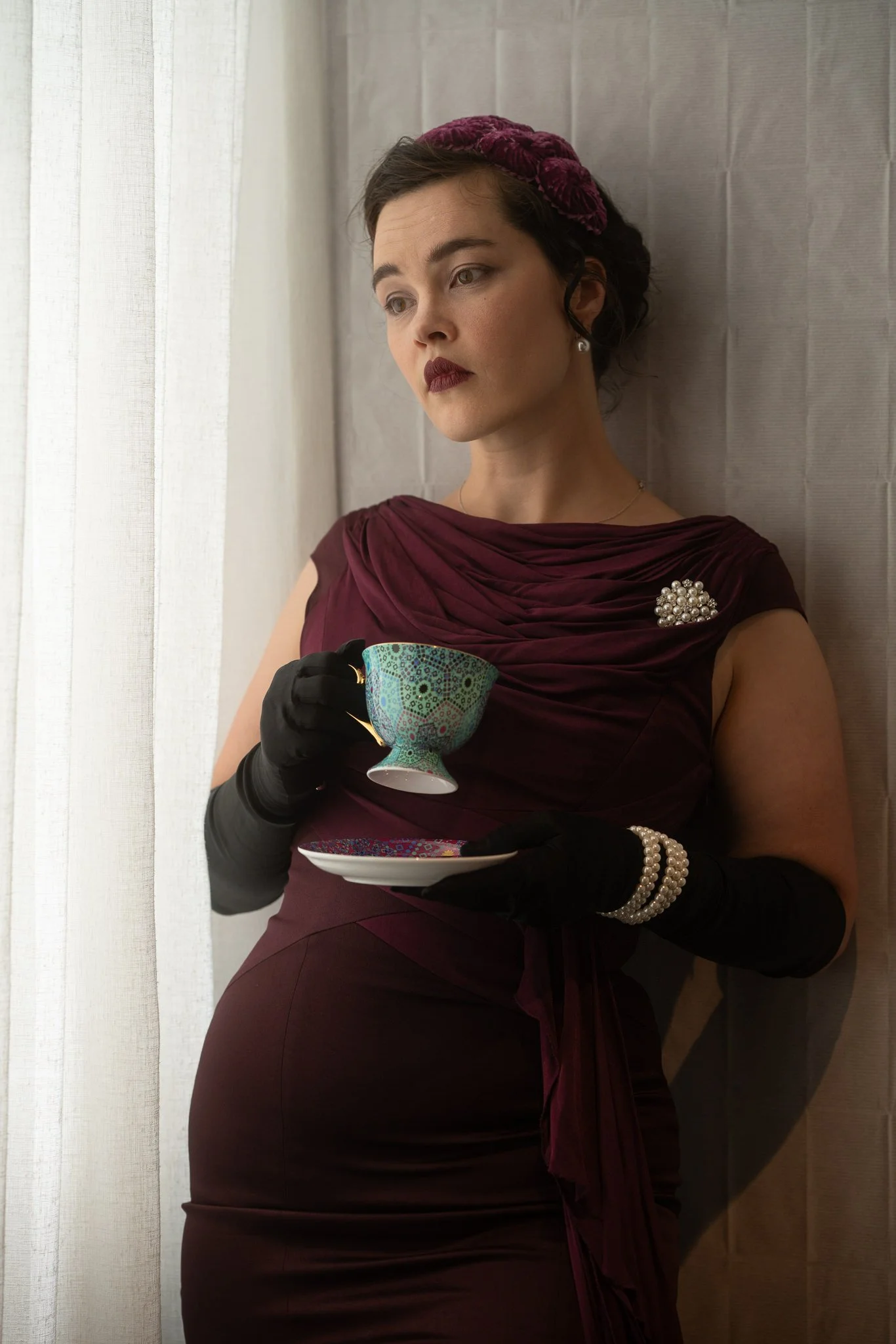 Anita looks at the camera holding a teacup in soft window light