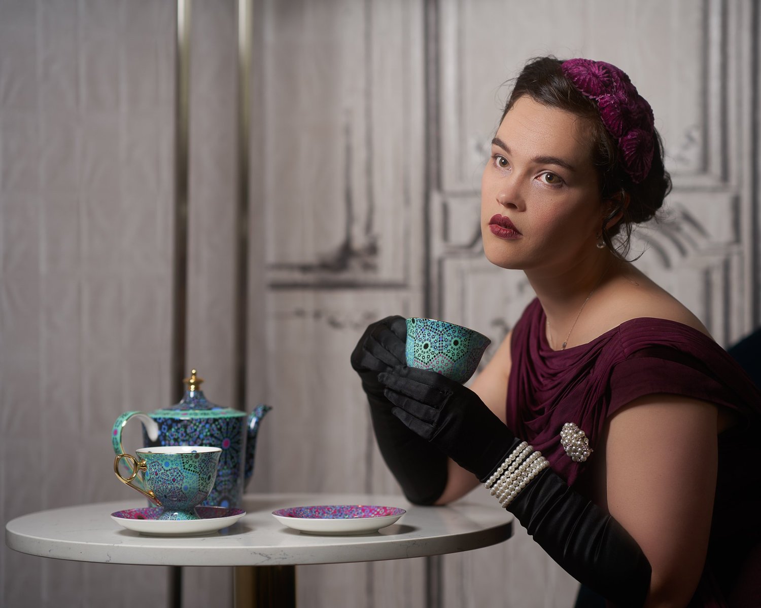 Anita at a small table with a teapot, holding a teacup