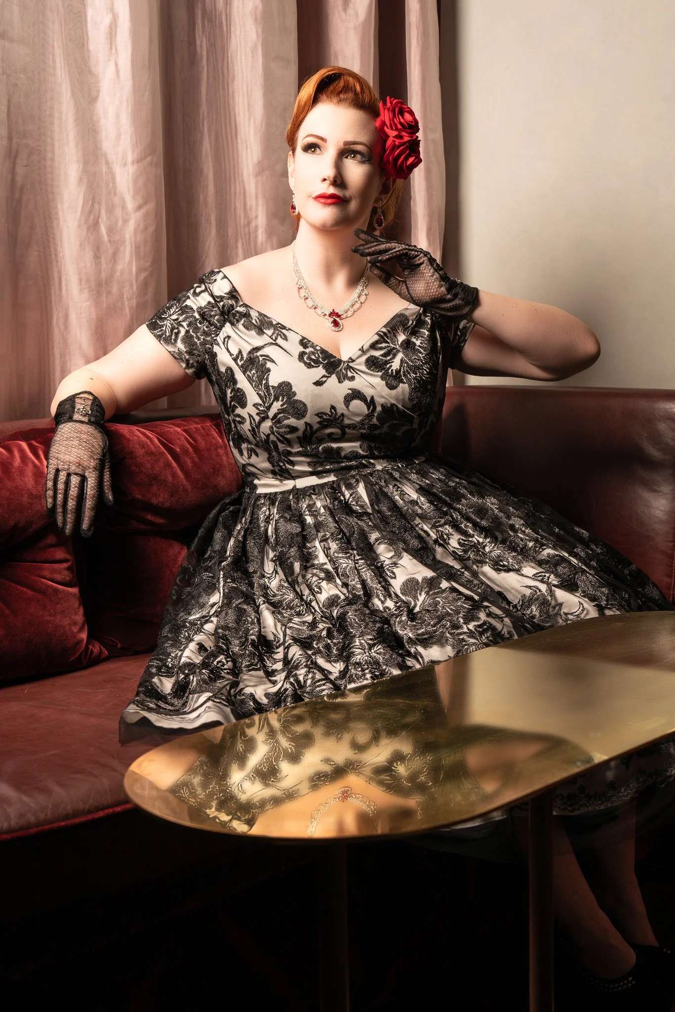 Jasmine poses in a lace dress and gloves in a red leather booth