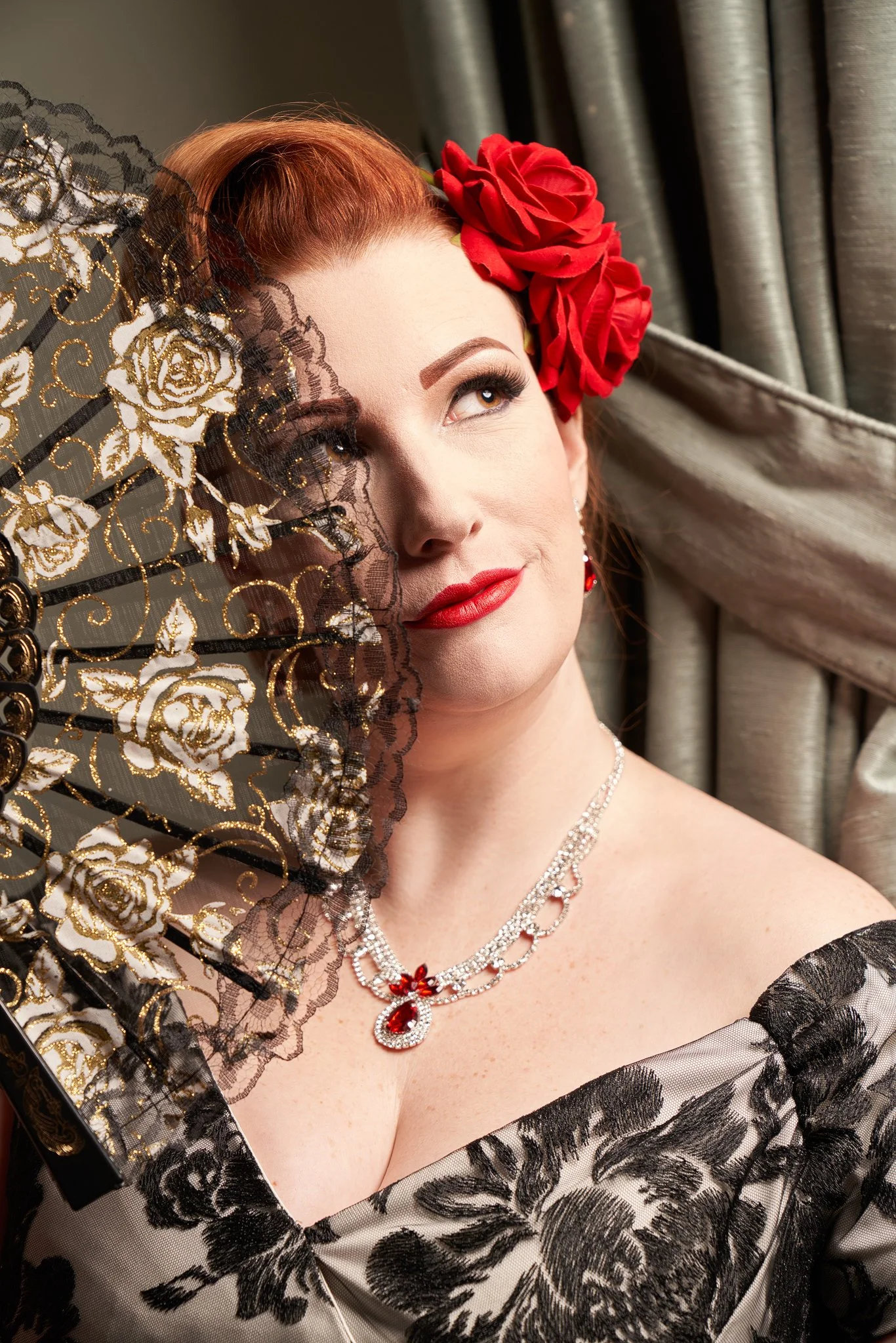 Jasmine with a red rose in her hair peeks over a lace fan