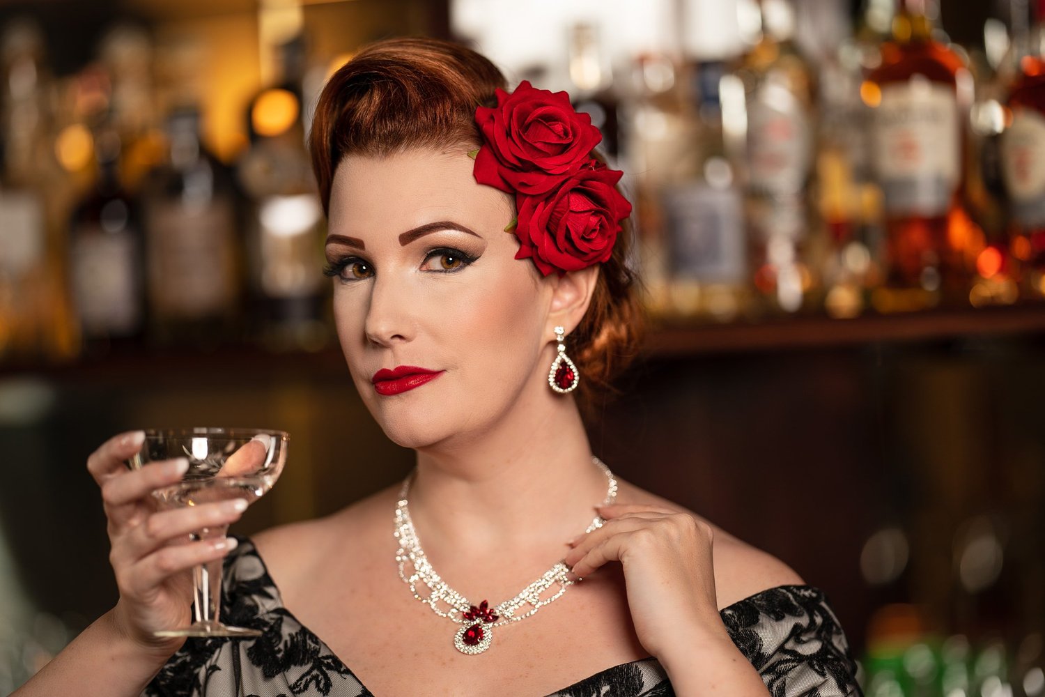 Jasmine holds a coupe glass with the bar lights glowing behind