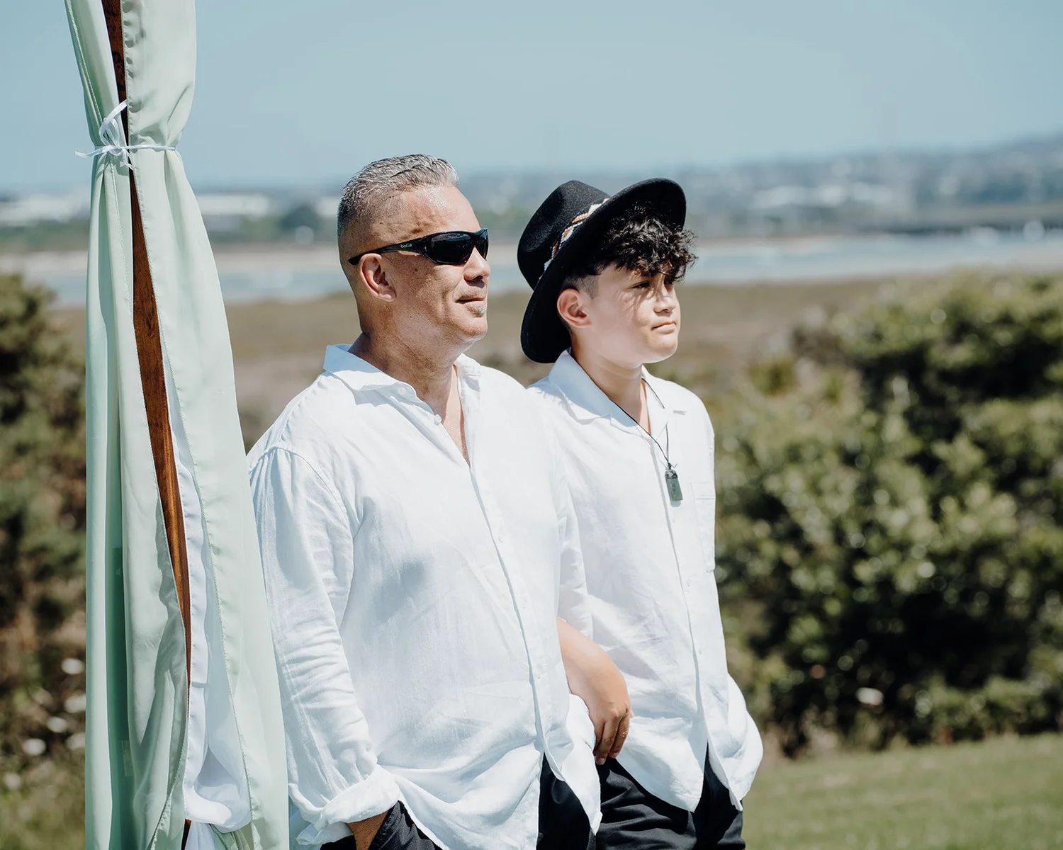 Shane and a groomsman in white shirts wait by the water on the Te Atatu Peninsula