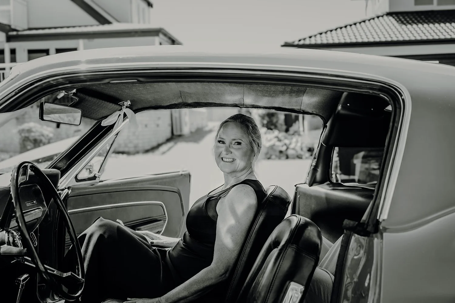 Black and white photo of Raewyn smiling from inside a classic car