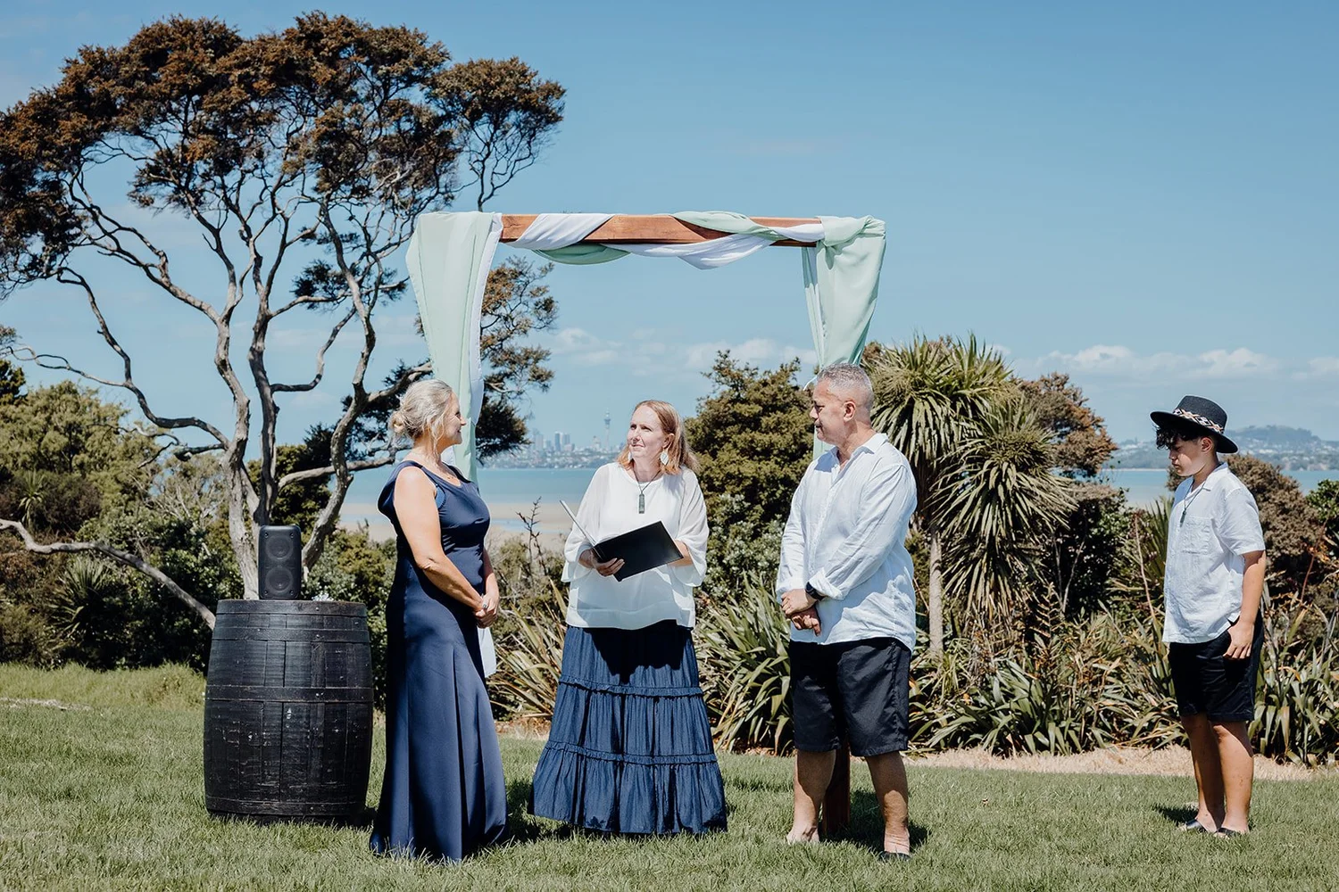 Raewyn and Shane exchange vows with the celebrant under a pōhutukawa