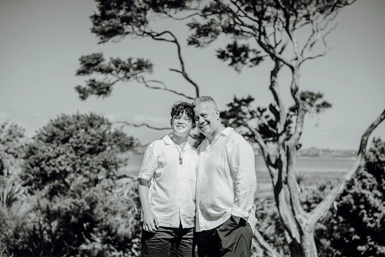 Black and white photo of two guests beneath a pōhutukawa tree