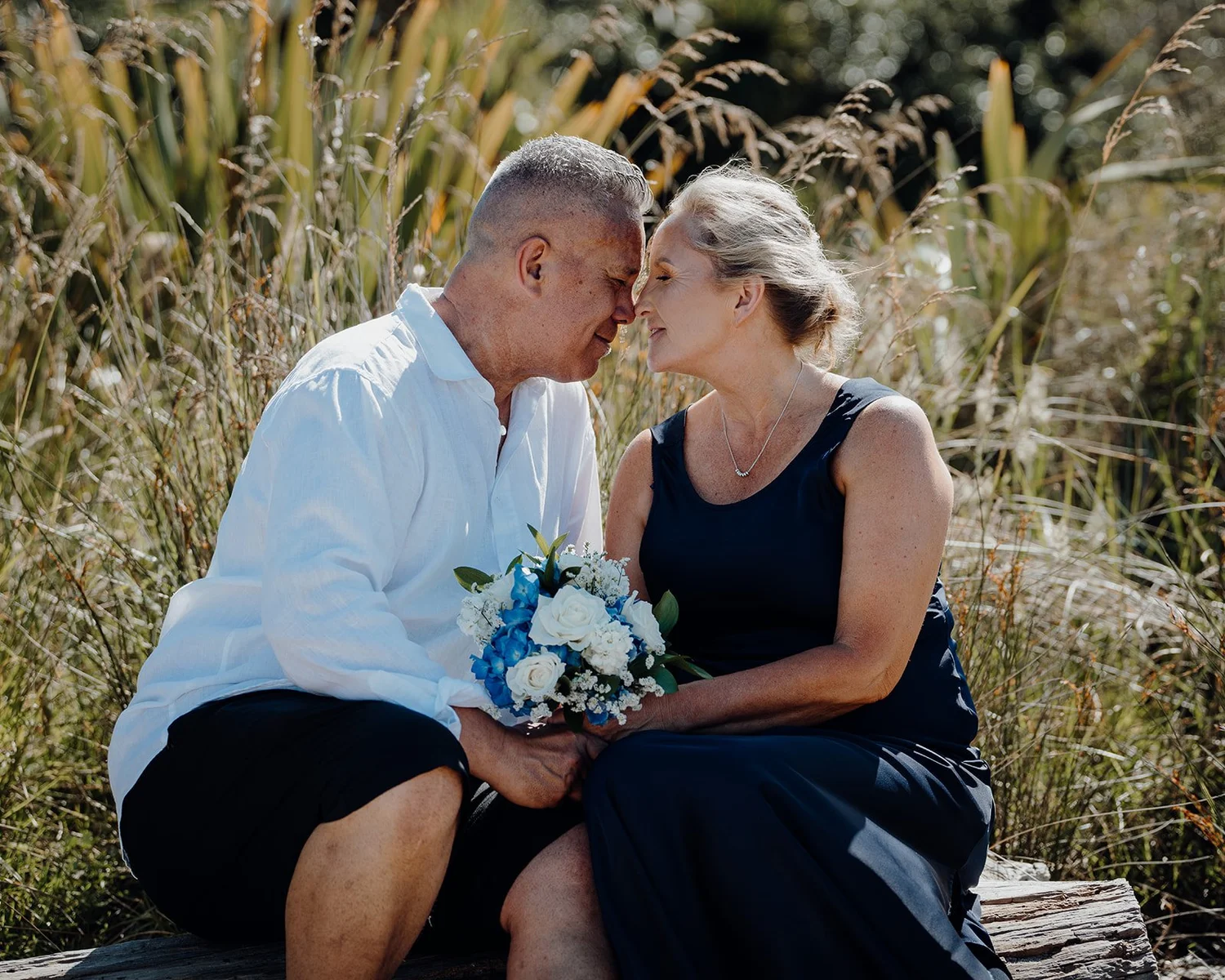 Raewyn and Shane touch foreheads seated among grasses