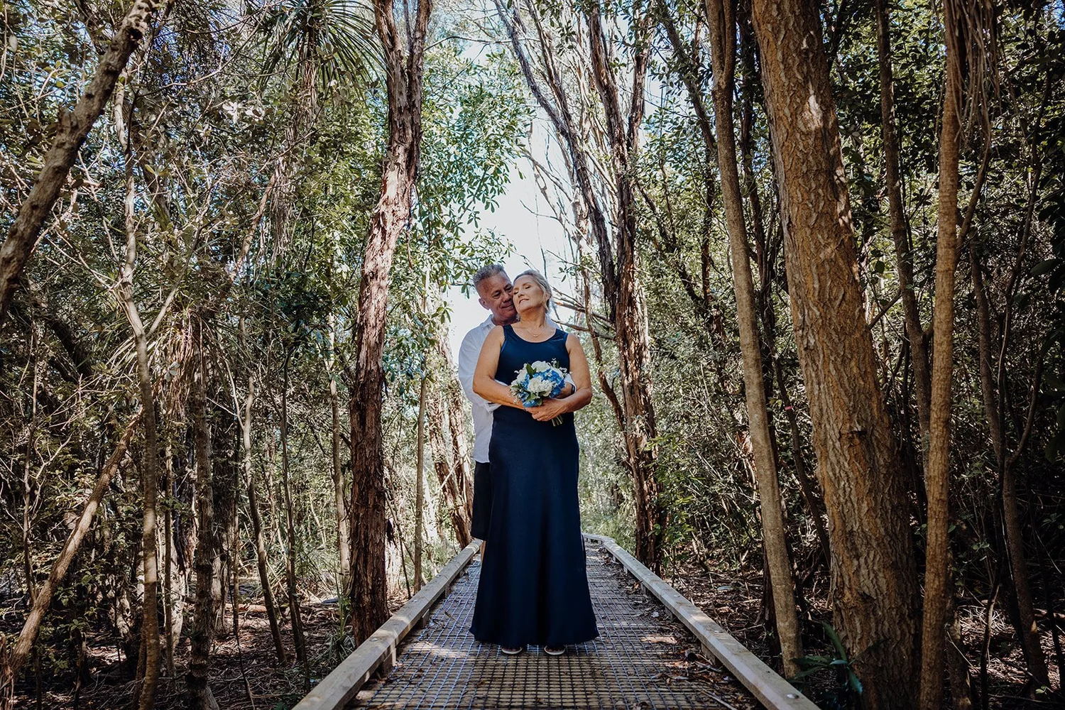 Raewyn and Shane embrace on a boardwalk through the trees