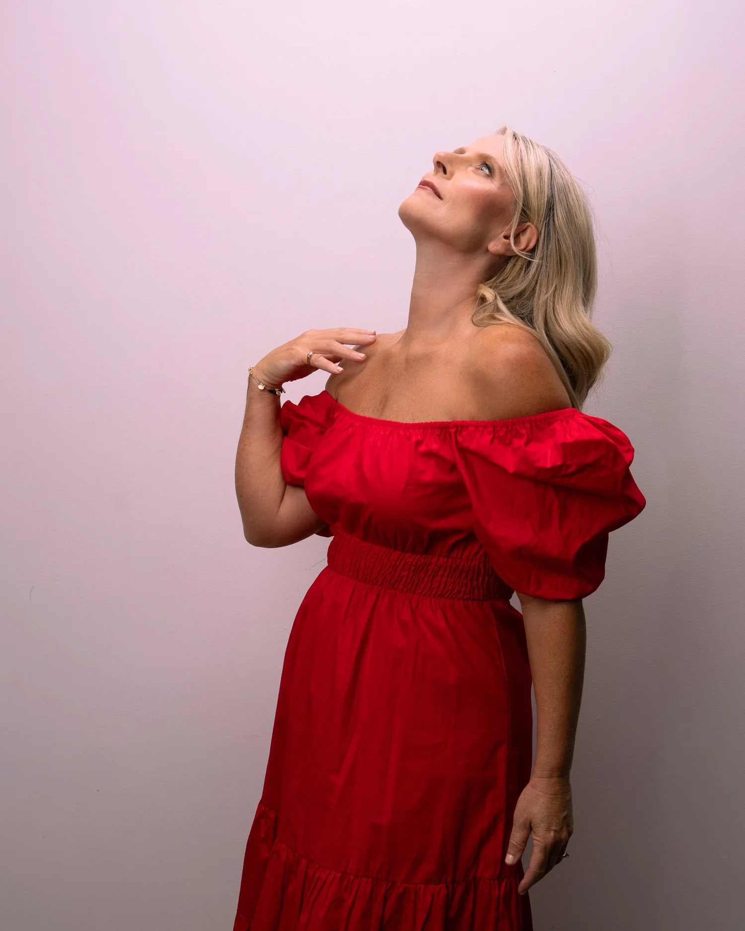 Ivanka in a red dress looks upwards against a pink backdrop