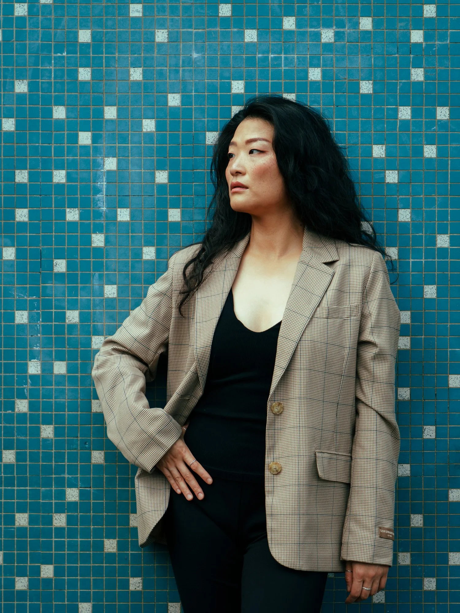 Anna in a checked blazer against a blue mosaic tile wall