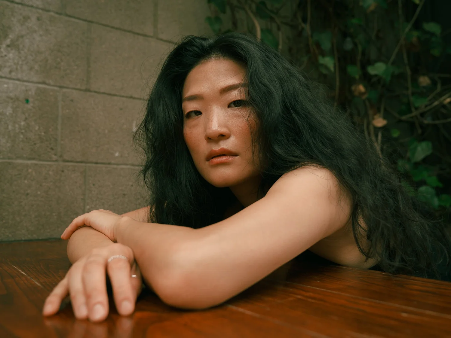 Anna leans on a table in front of an ivy-covered wall