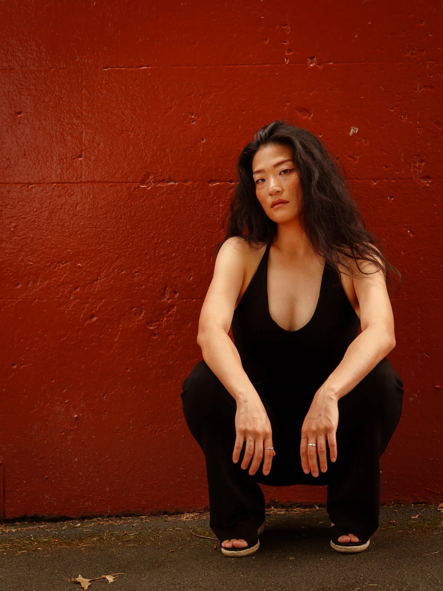 Anna crouches in front of a deep red wall