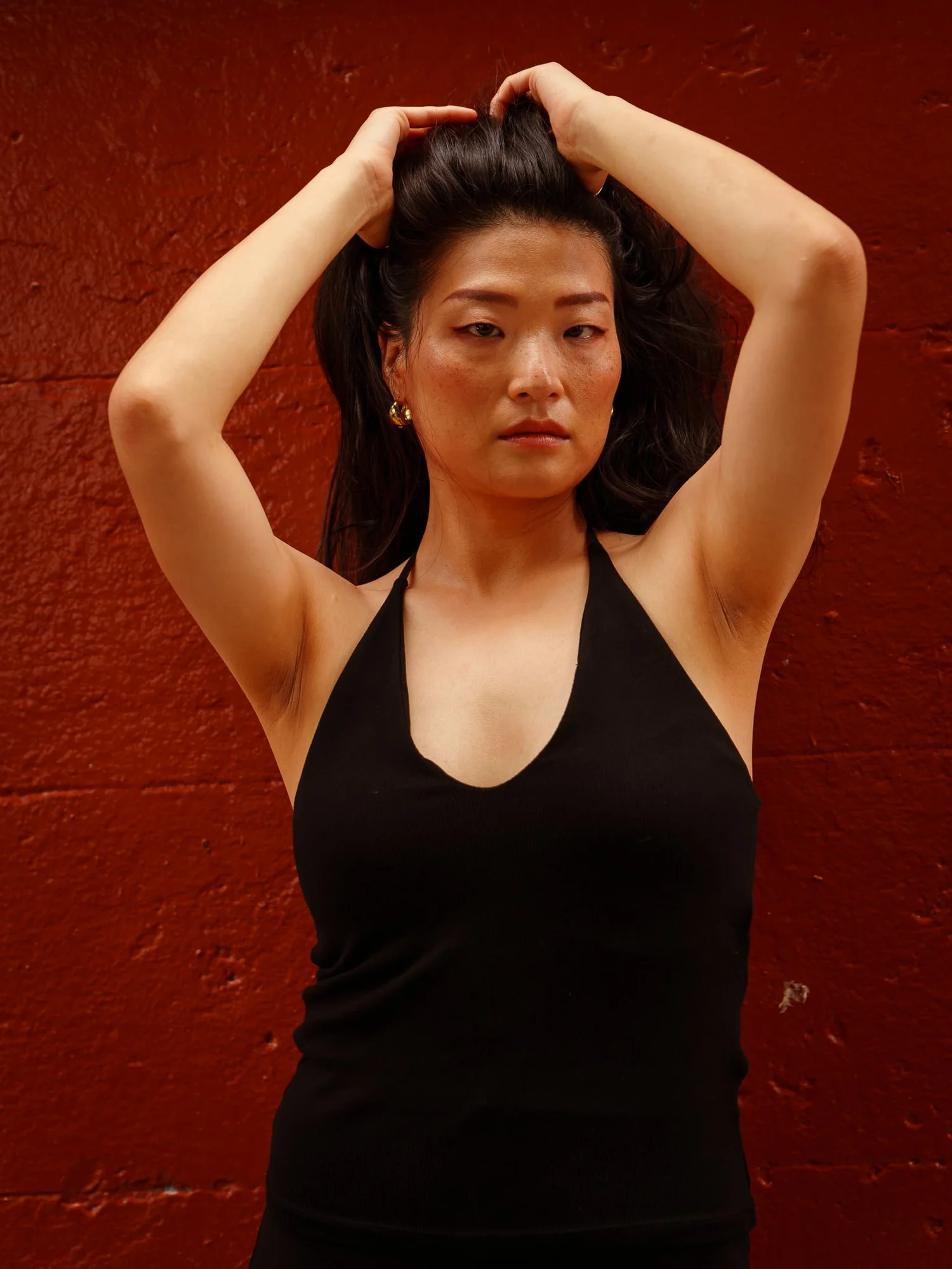 Anna with both hands in her hair in front of a red wall