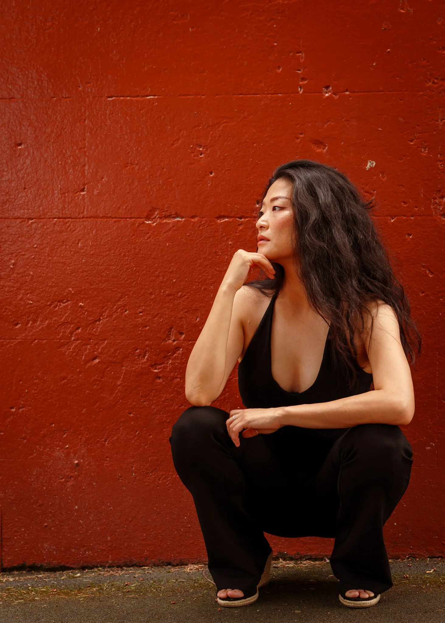 Anna crouches and rests her chin on her hand against a red wall