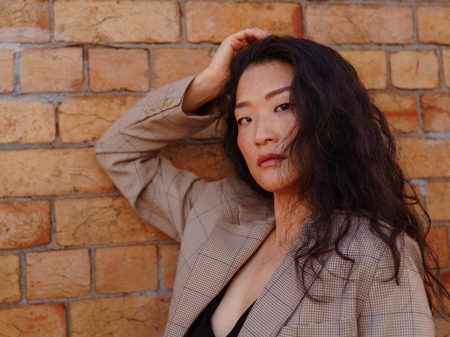 Anna in a checked blazer leaning on a brick wall