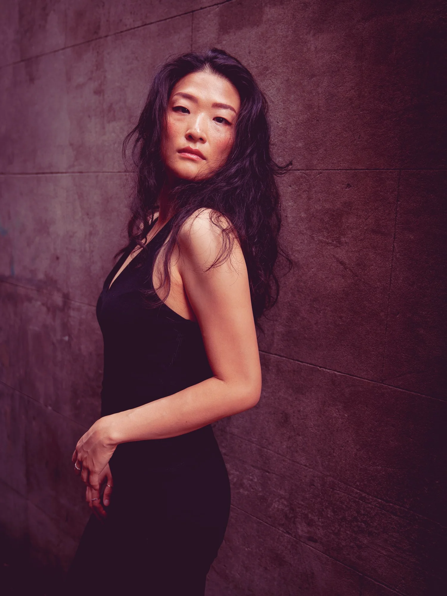 Anna glances over her shoulder against a dark textured wall
