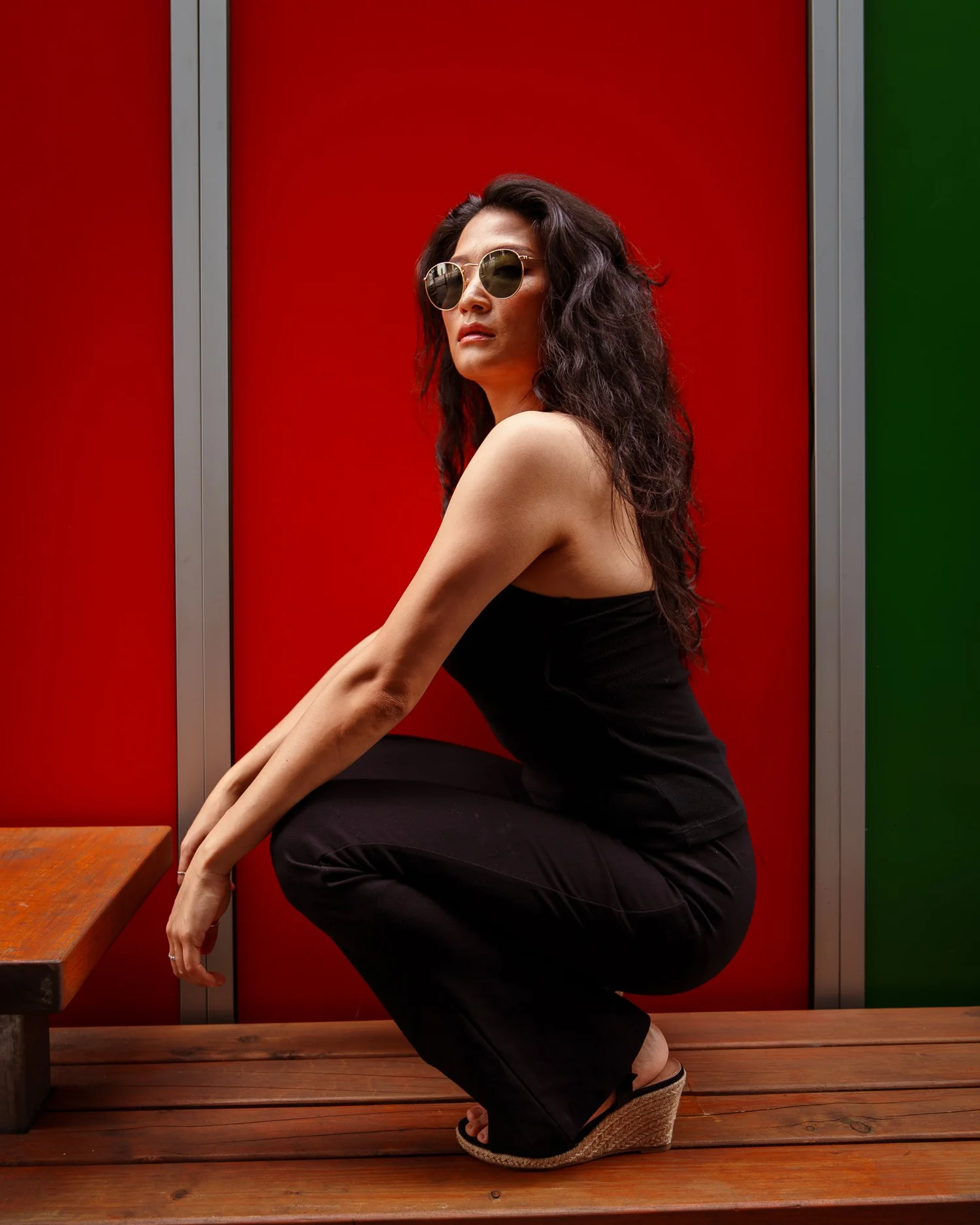 Anna in sunglasses crouching on a bench beside a red door