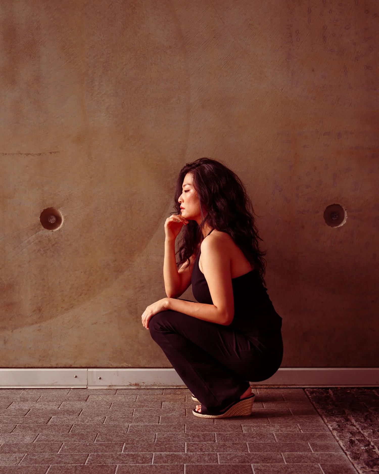 Anna crouches in profile against a smooth concrete wall