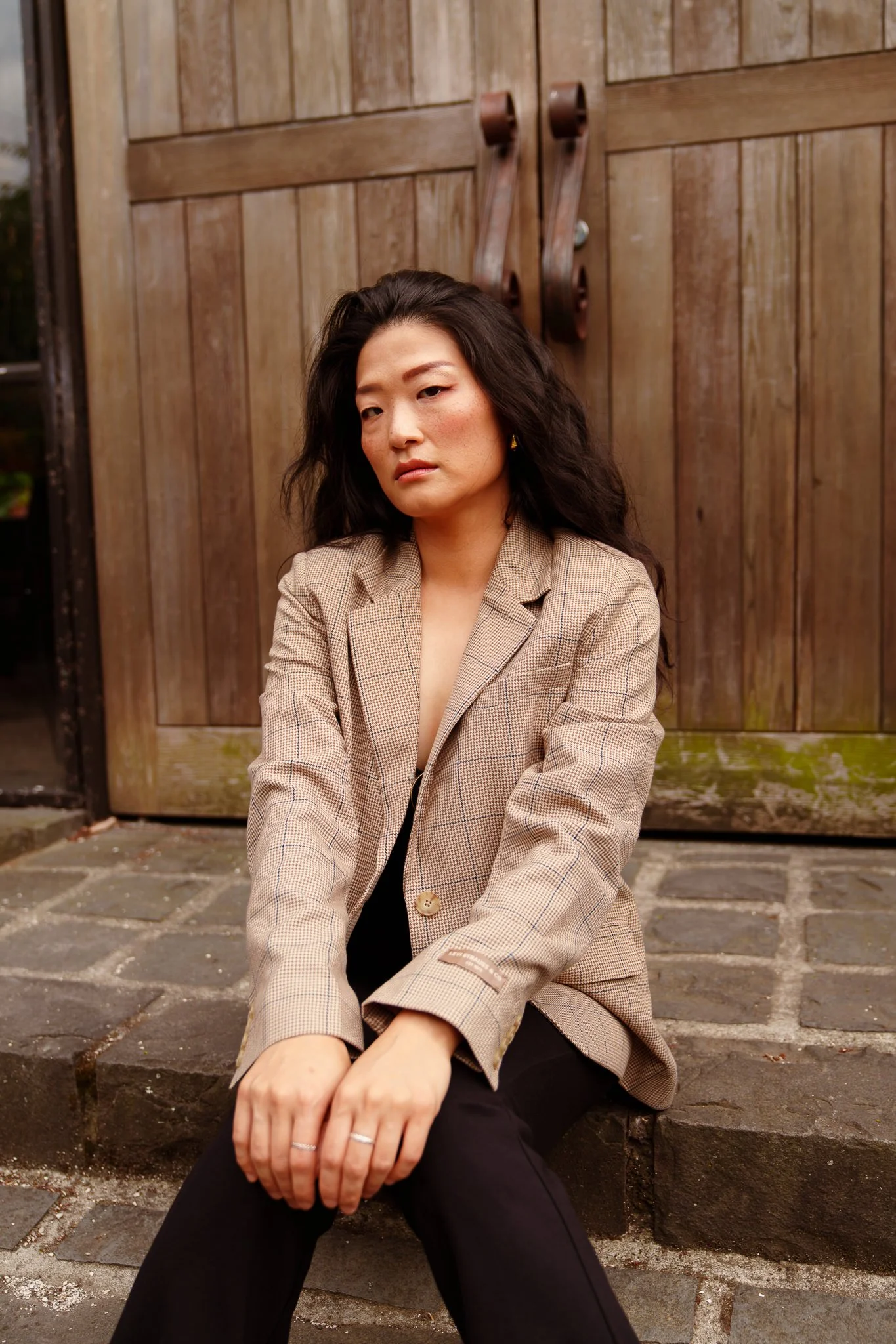 Anna sits in front of an old wooden gate in a checked blazer