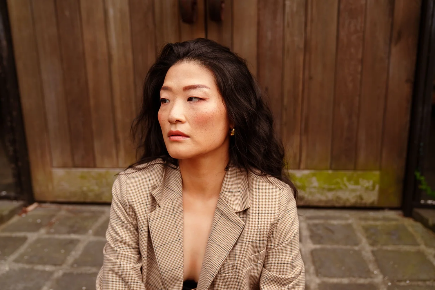 Anna in a beige blazer sitting in front of a wooden gate