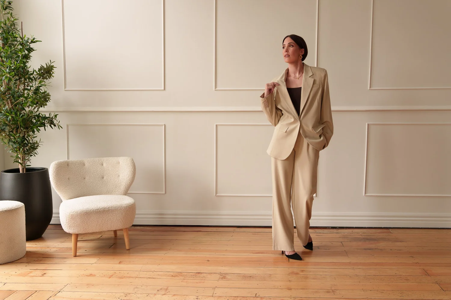 Nat walks across a timber floor in a cream suit