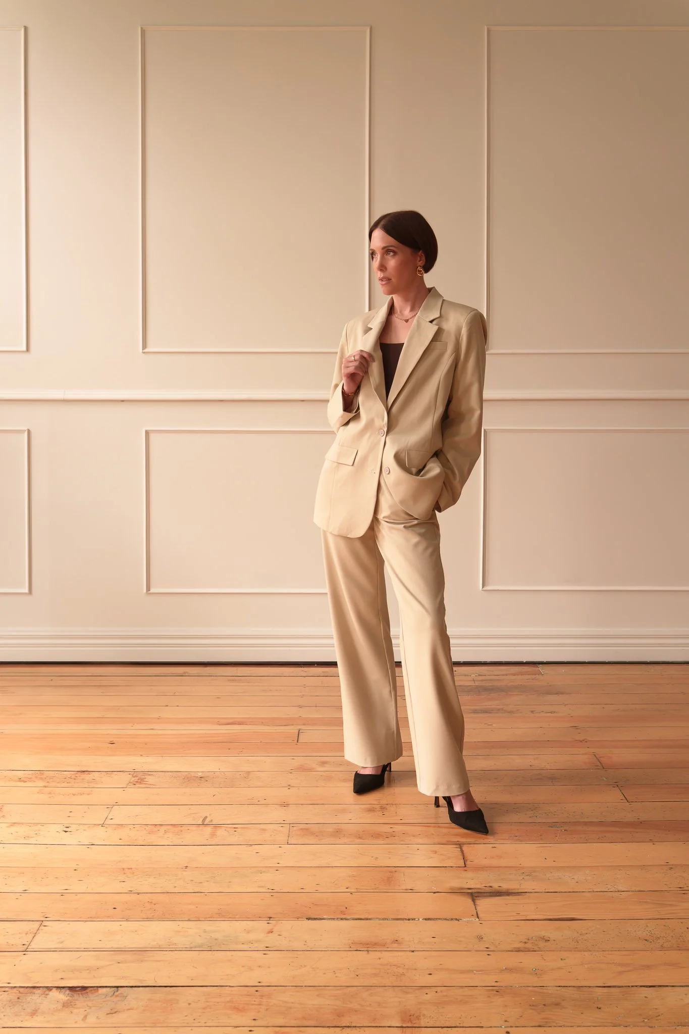 Nat with one hand in her pocket in a cream suit