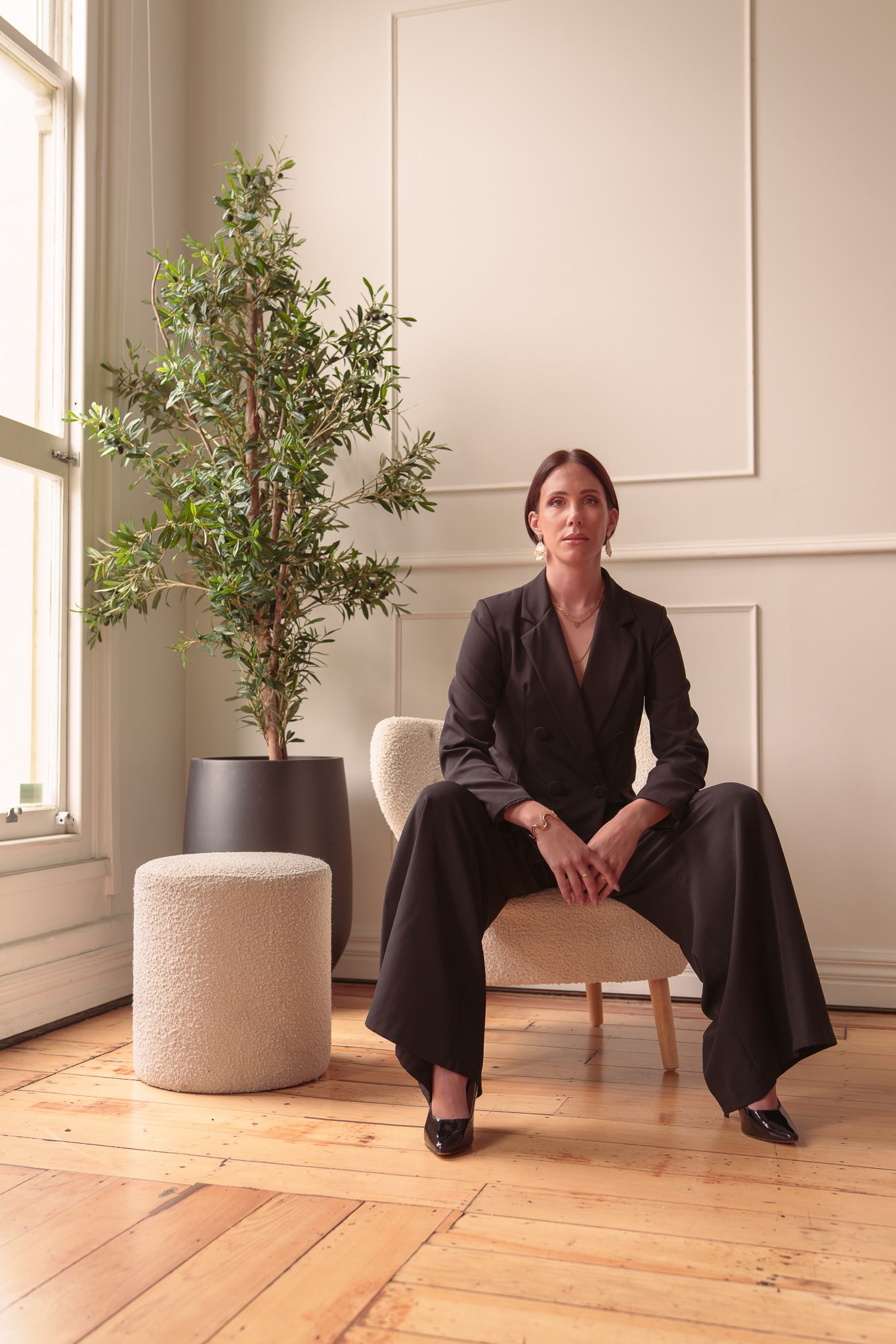 Nat in a black suit seated beside a potted olive tree