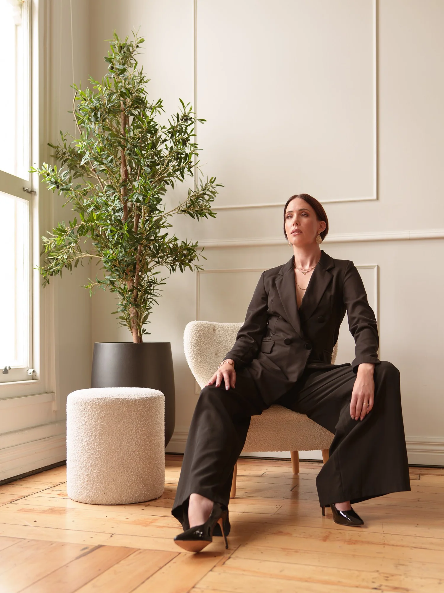 Nat leans back in a chair in a black suit