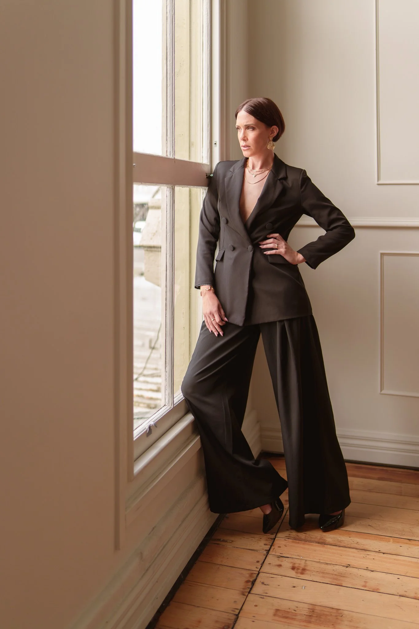Nat in a black suit leaning by a tall window