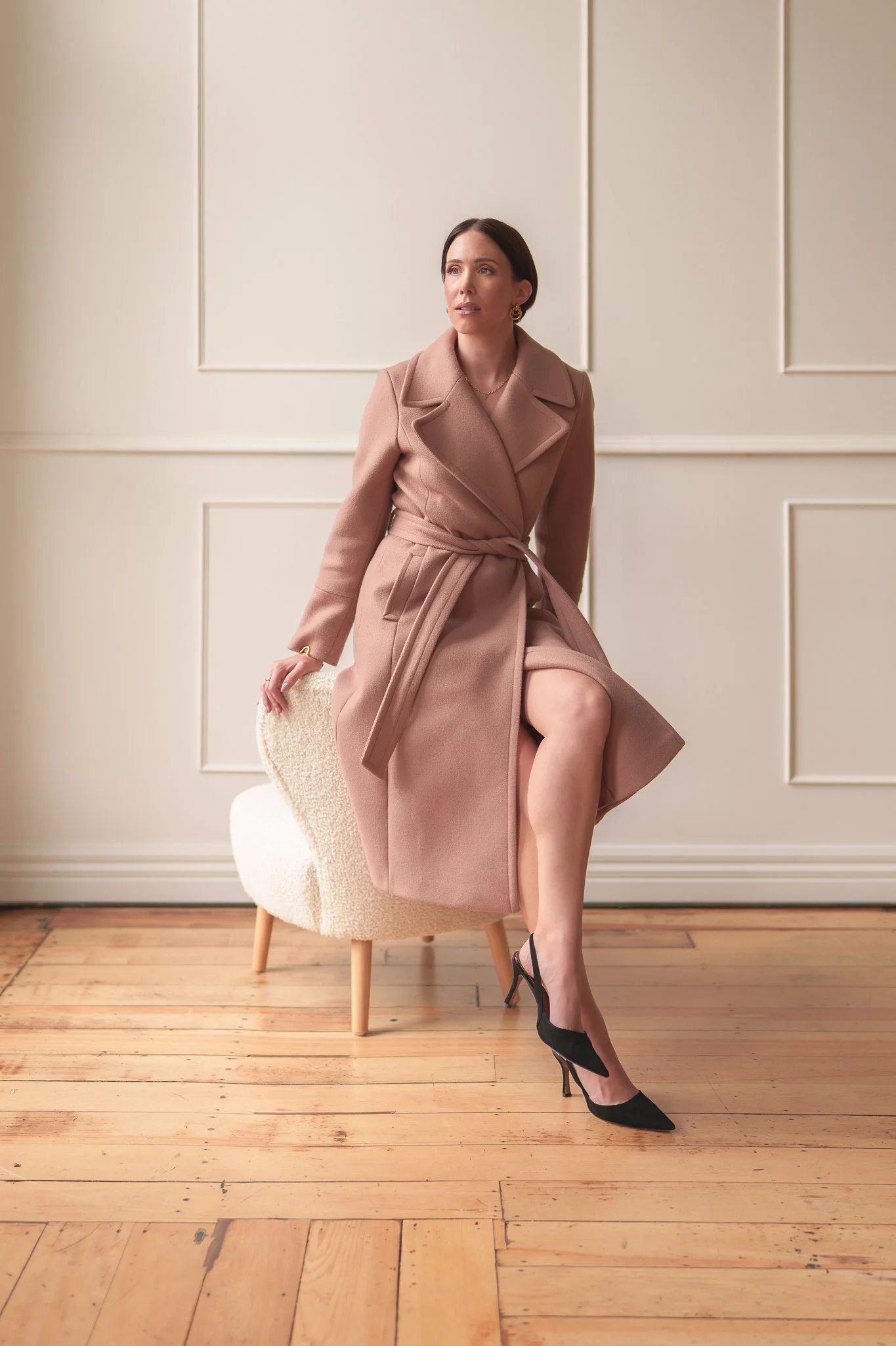 Nat perches on the arm of a chair in a blush coat