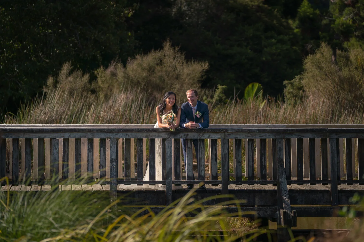 Gel and James on a wooden bridge surrounded by tall grasses