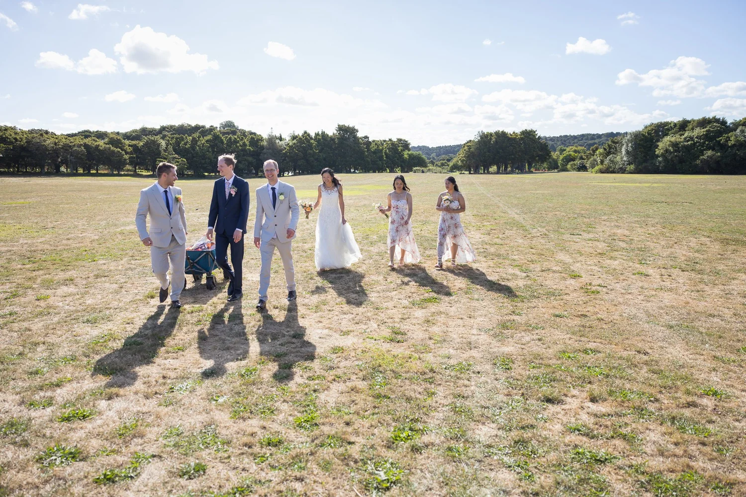 Gel and James walk across an open field with their bridal party