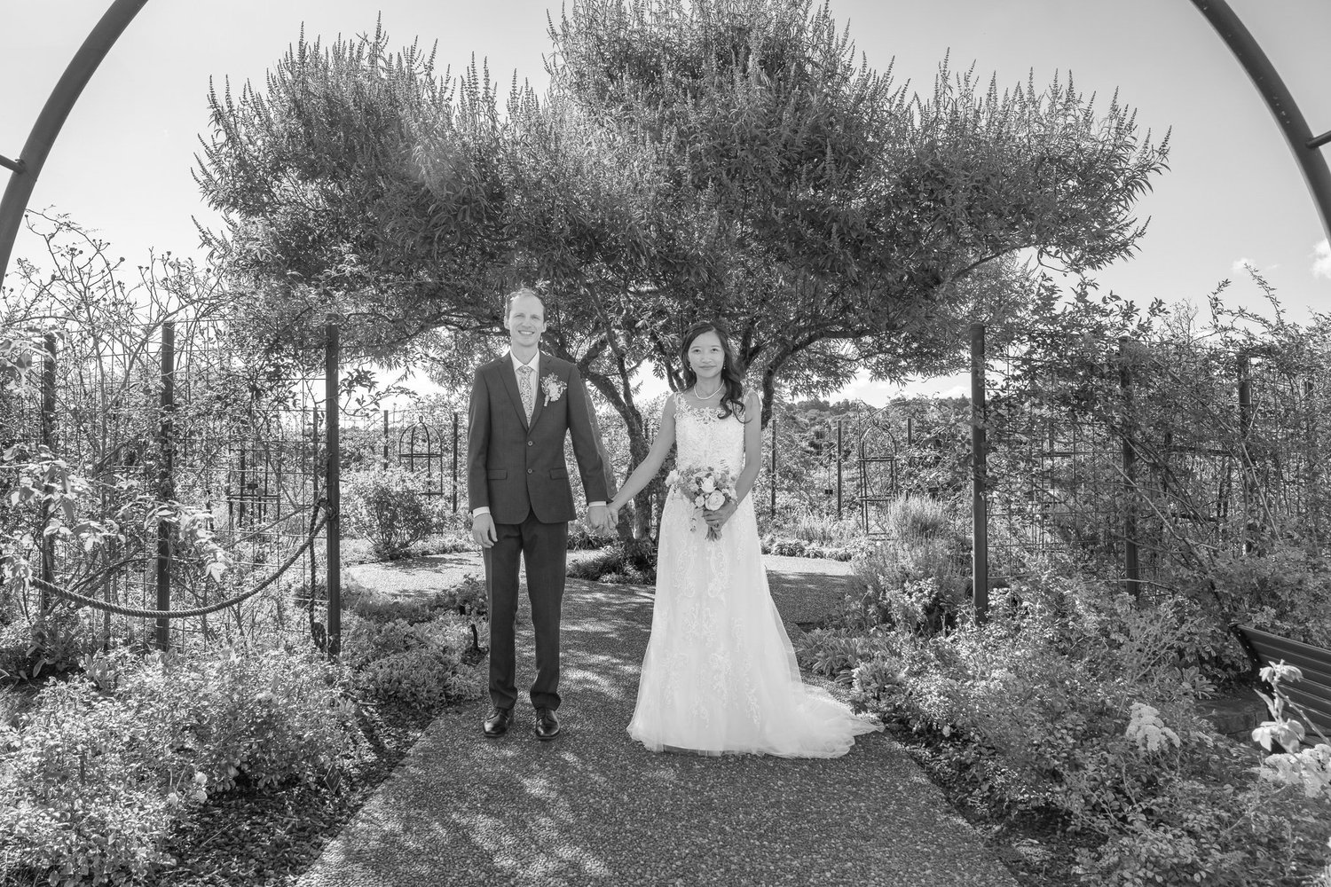 Black and white photo of Gel and James beneath an olive tree in a walled garden