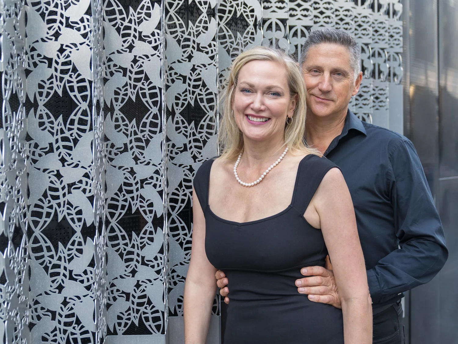 The couple embrace in front of a decorative wall