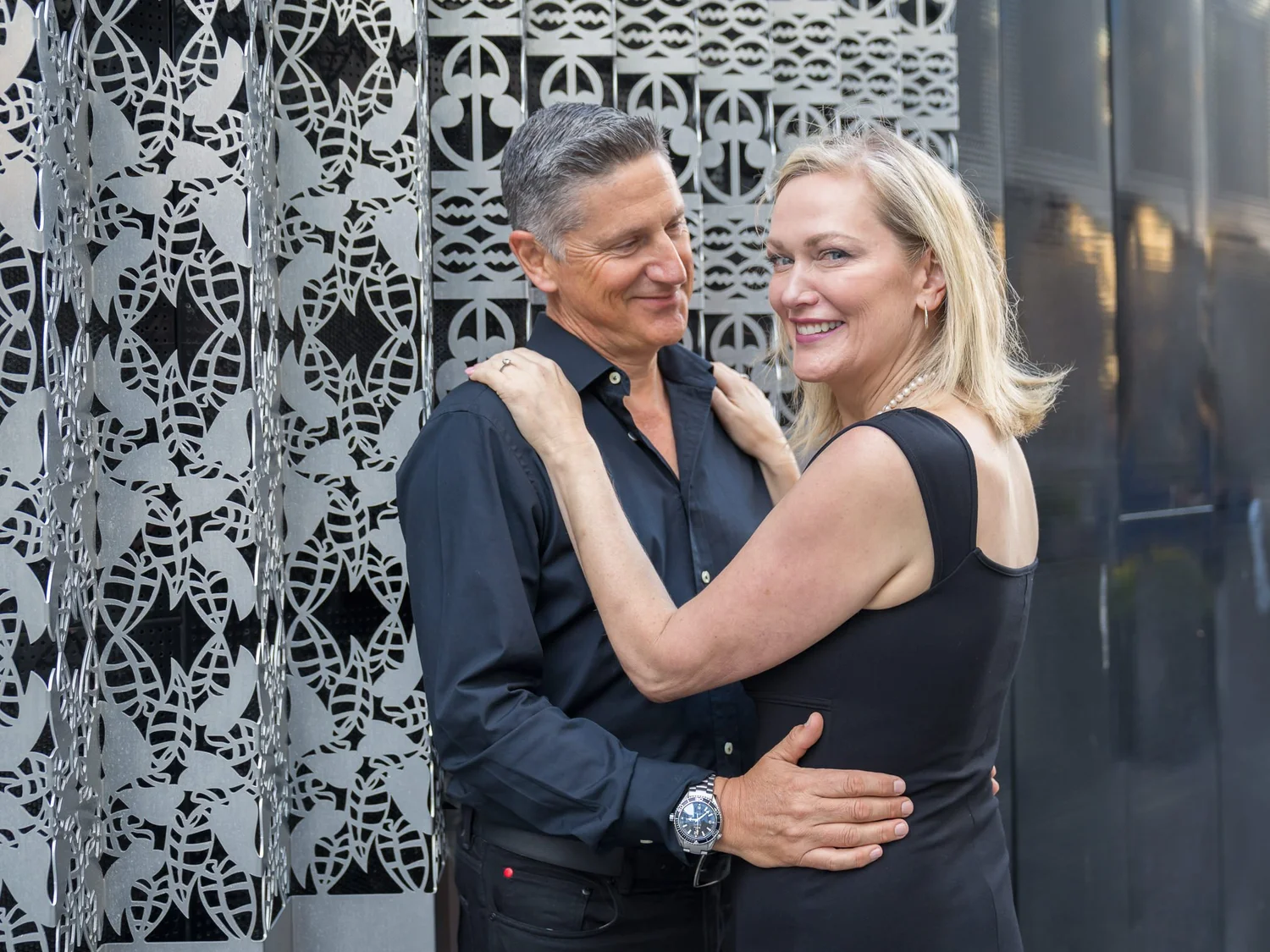 The couple share a close embrace against a patterned wall