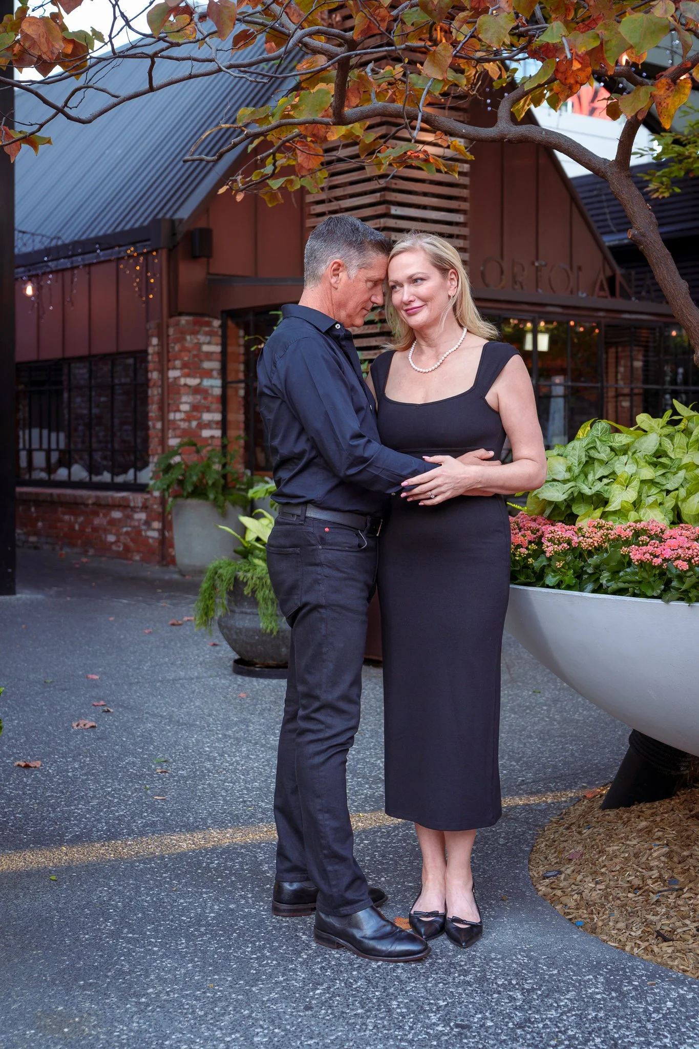 The couple embrace beside planters under autumn trees