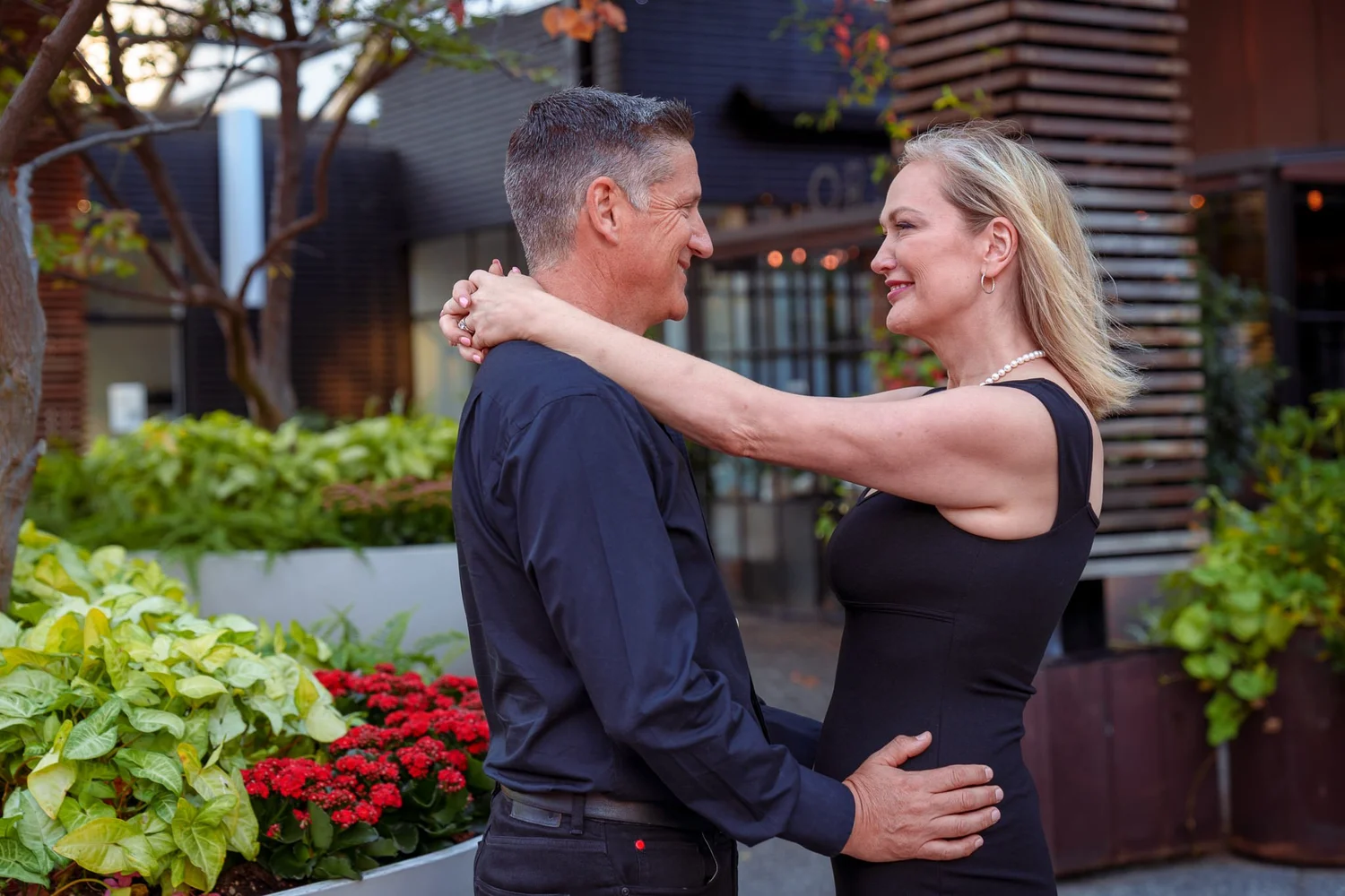 The couple share a laugh beside red flowers