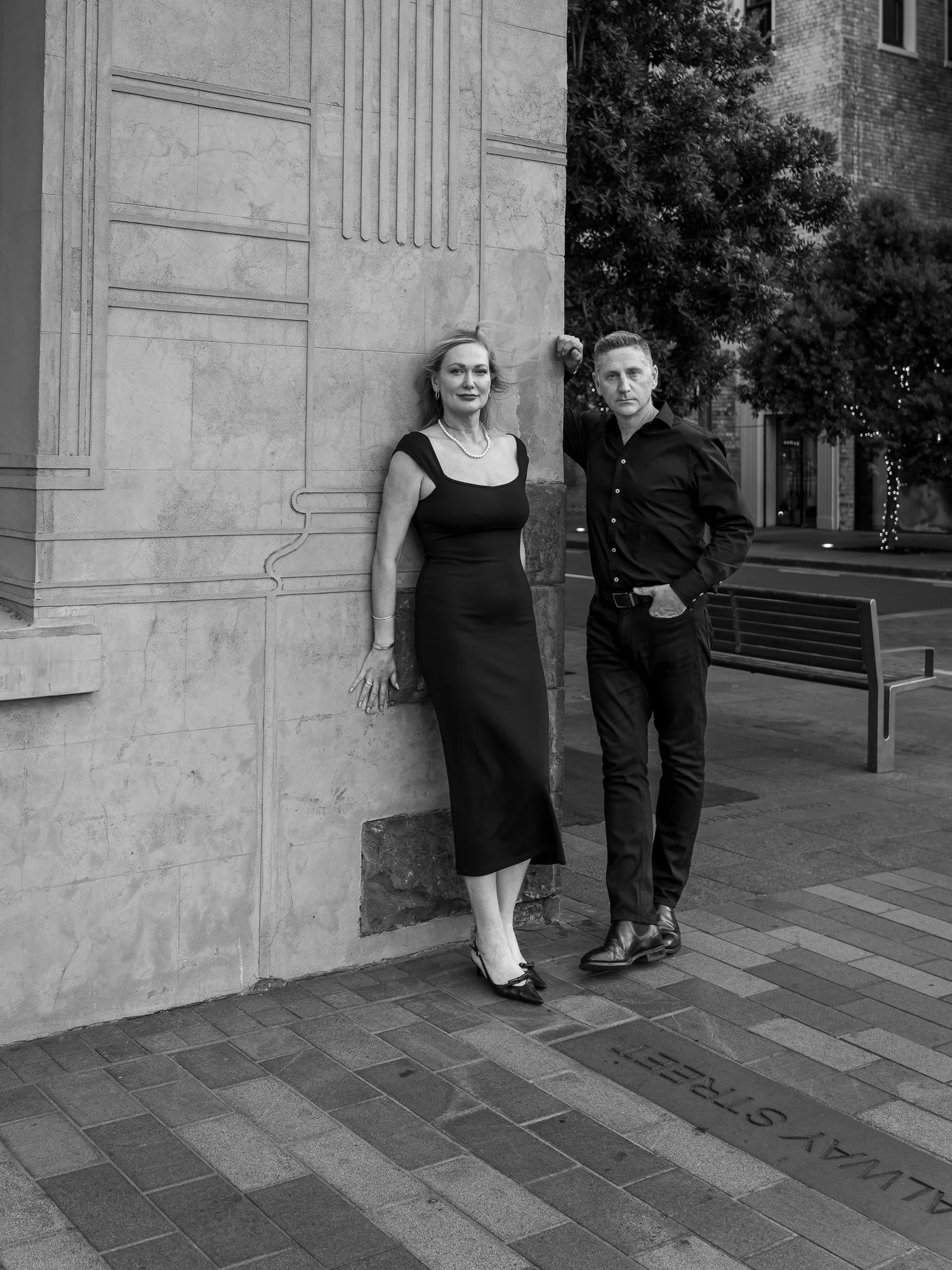 Black and white photo of the couple leaning against a stone building