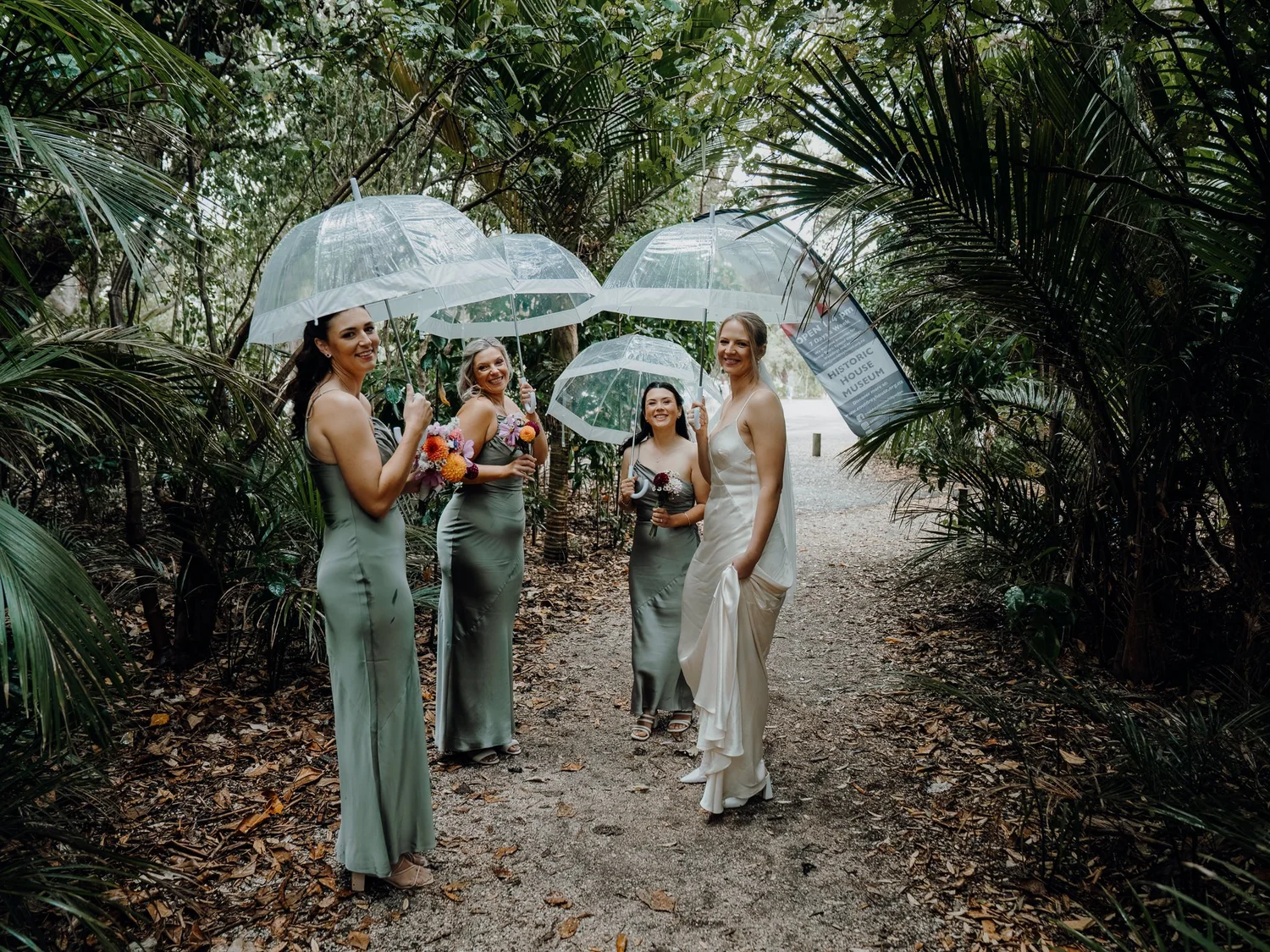 The bridesmaids under clear umbrellas on a bush path
