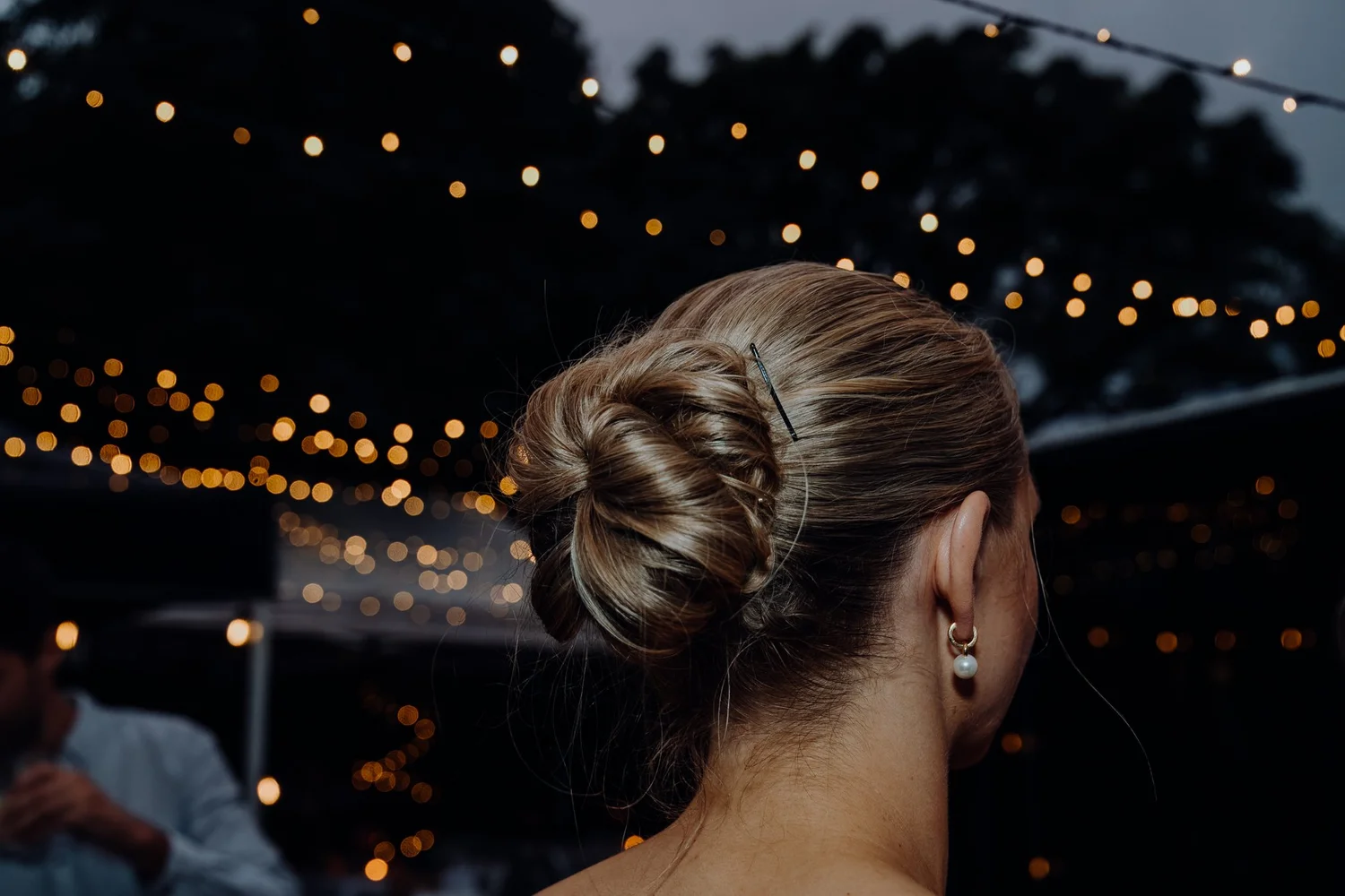 The back of a guest's updo with fairy lights beyond