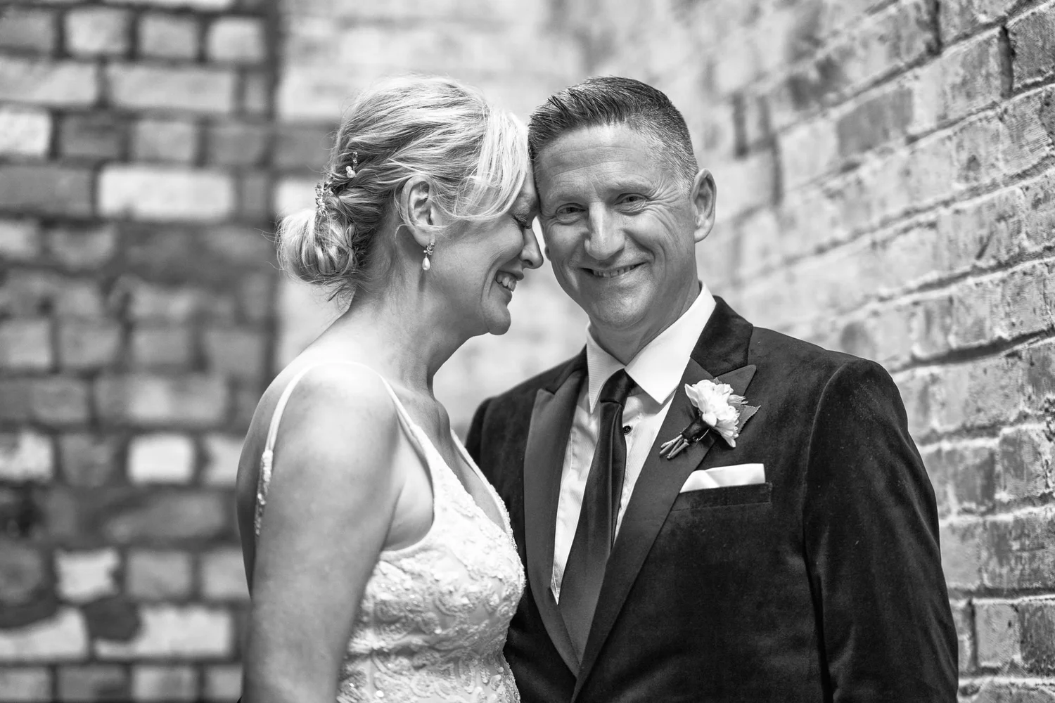 Black and white photo of the couple laughing by a brick wall